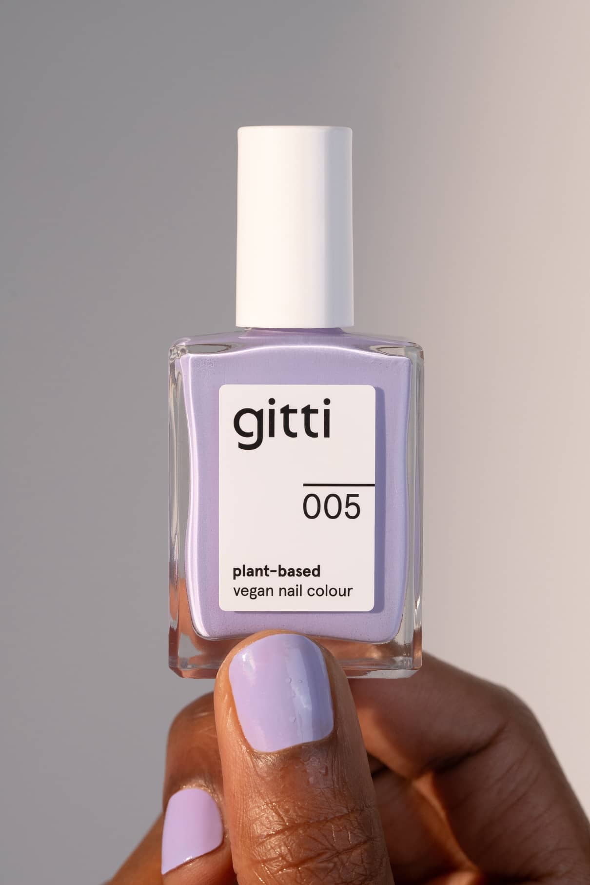 Eine Hand mit lavendelfarben lackierten Nägeln hält eine Flasche gitti no. 005, einen veganen, pflanzenbasierten Nagellack in harmonischem Lila.