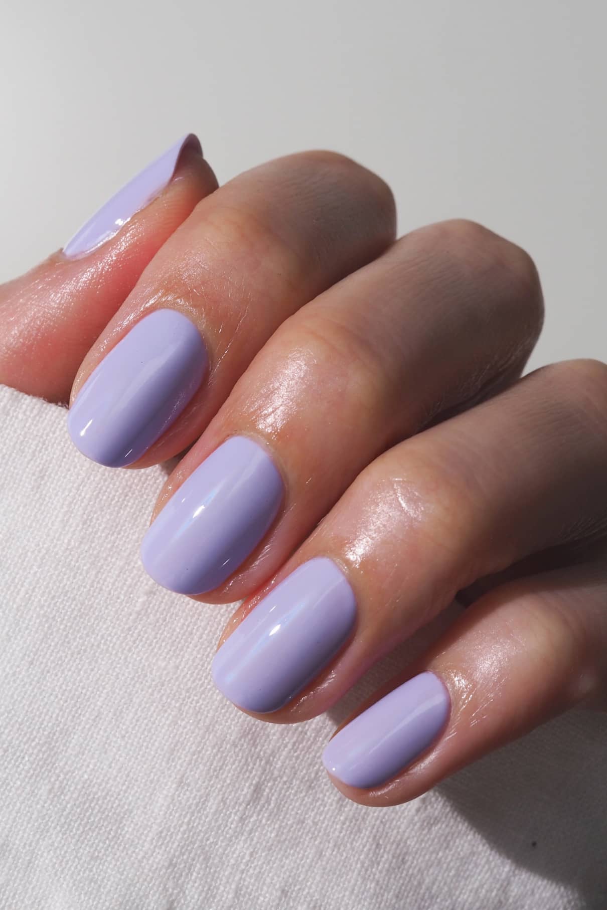 Nahaufnahme einer Hand mit sauber manikürten Nägeln, die in gitti no. 005, einem harmonischen violetten Farbton, der auf einer weißen Fläche ruht.
