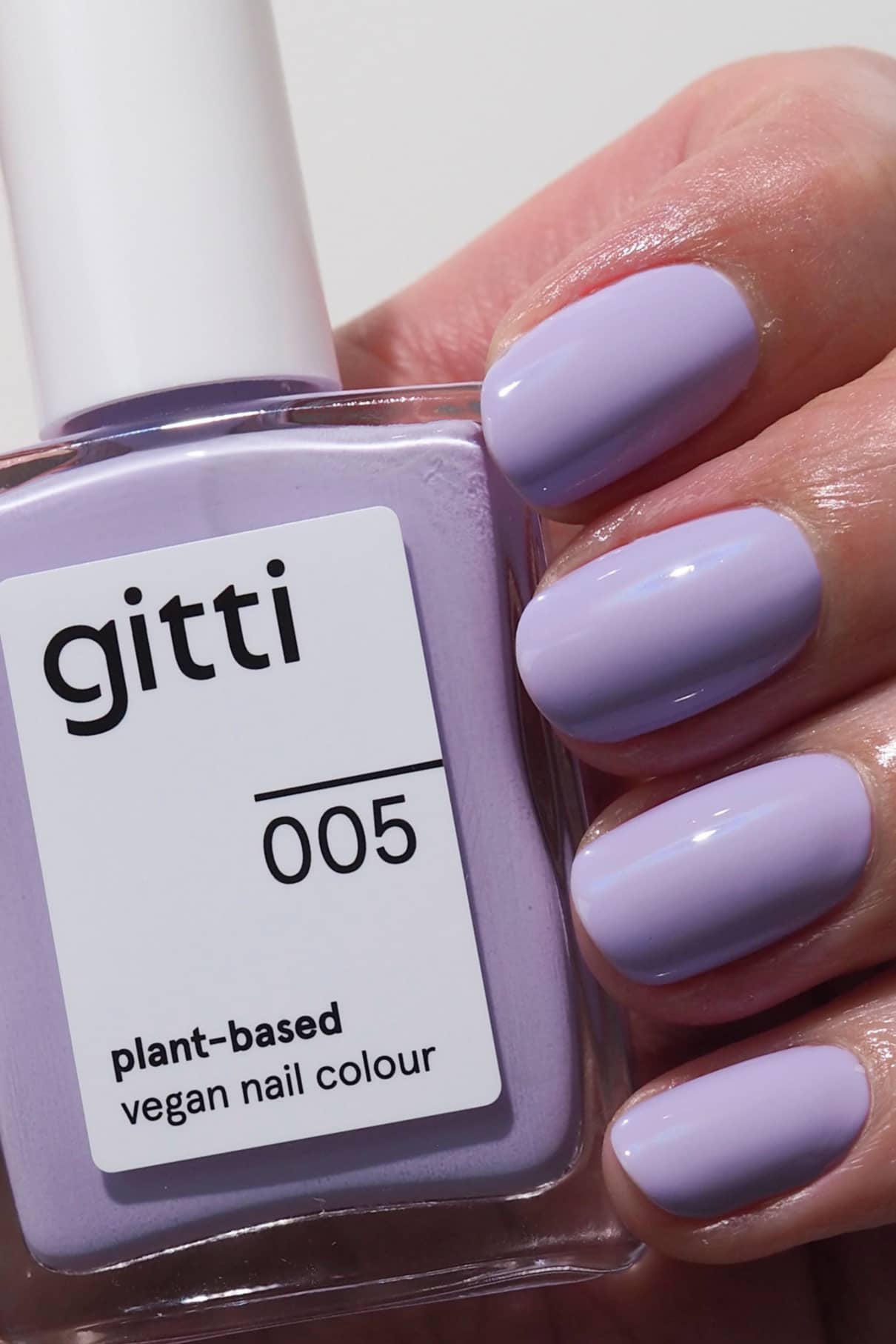 Eine Hand mit sauber manikürten, in einem harmonischen Lila-Ton lackierten Nägeln hält eine Flasche gitti no. 005, einem veganen Nagellack auf Pflanzenbasis.