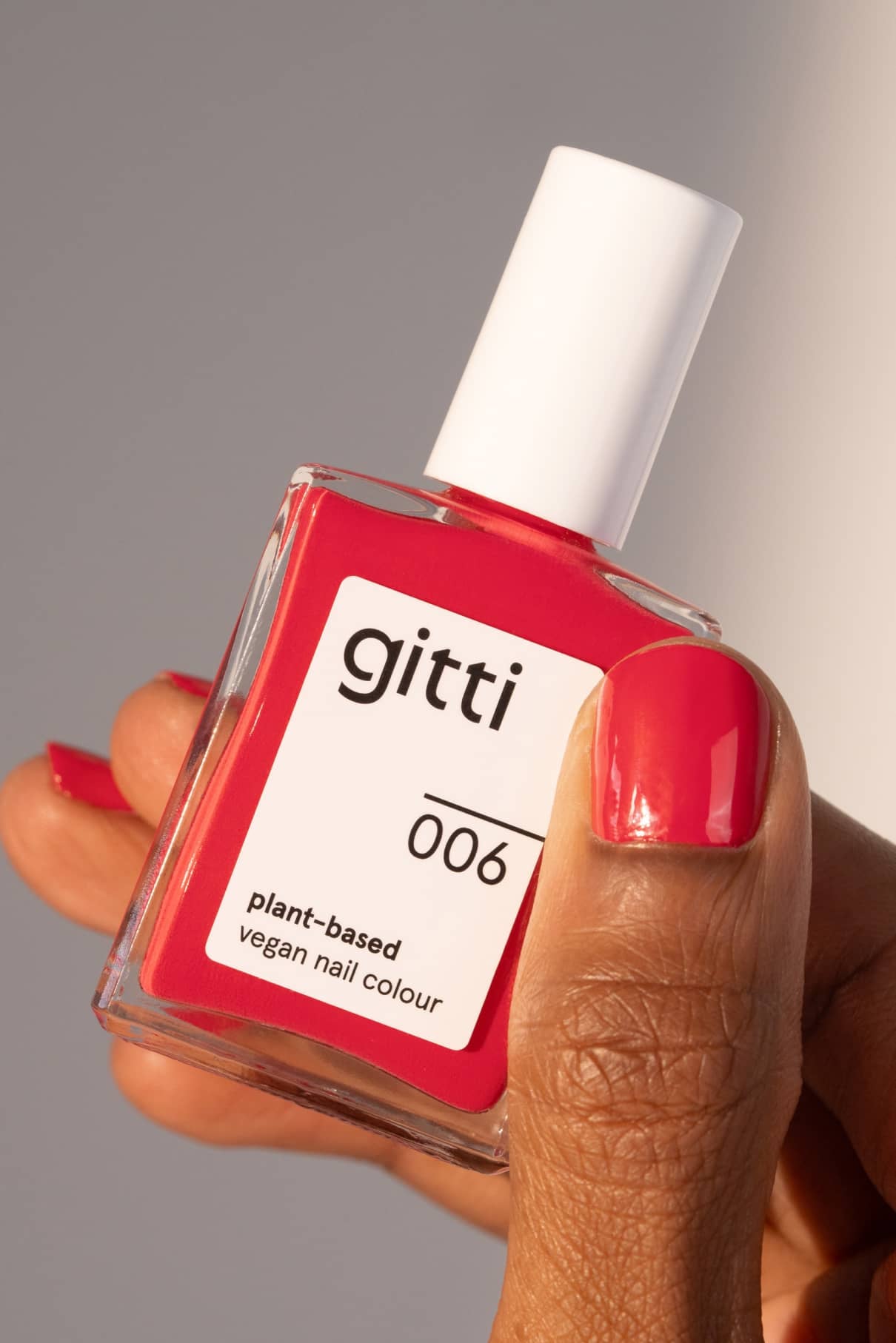 Eine Hand hält eine Flasche mit gitti no. 006 pflanzliche vegane Nagelfarbe. Die Nägel sind in einem passenden rosa Farbton mit rosa Unterton lackiert.