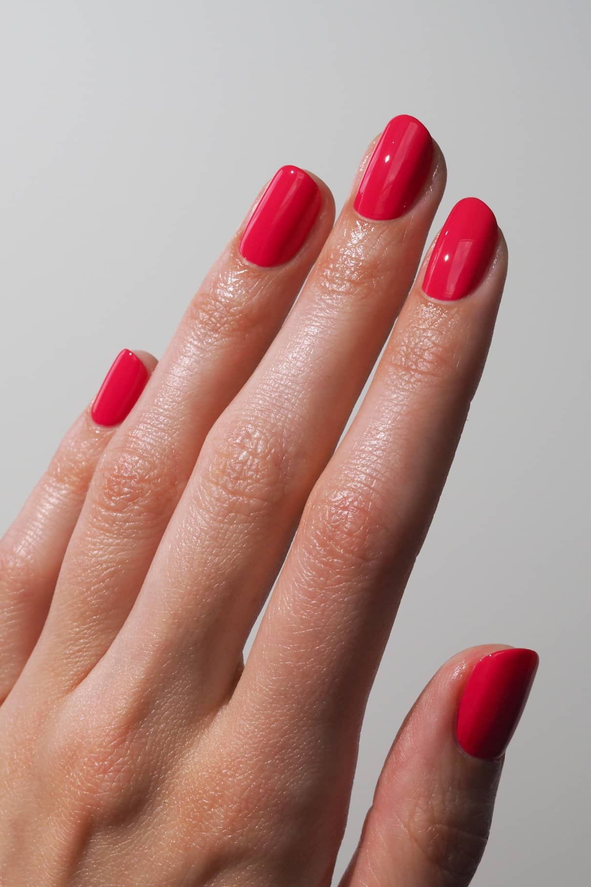 Nahaufnahme einer Hand mit sauber manikürten Nägeln, die in gitti no. 006 - ein leuchtendes Rot mit glänzendem Finish und rosa Untertönen - vor einem unifarbenen Hintergrund.
