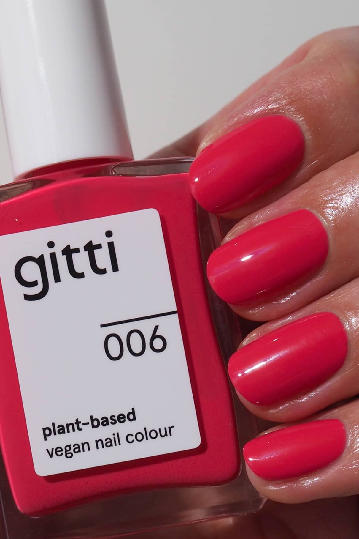 Eine Hand mit sauber manikürten, leuchtend rosa Nägeln hält eine Flasche gitti no. 006, einer veganen Nagelfarbe auf Pflanzenbasis, mit einem pinkfarbenen Unterton und einer verbesserten Formel für eine lebendige, lang anhaltende Farbe.