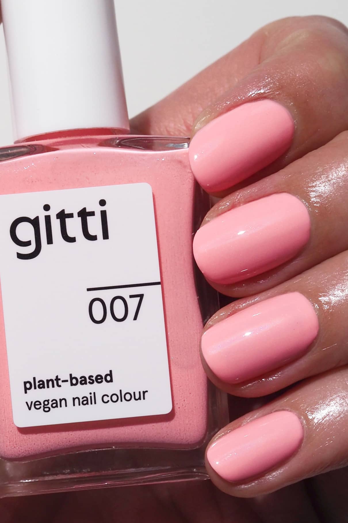 Eine Hand mit rosa lackierten Nägeln hält eine Flasche gitti no. 007 pflanzlicher, veganer Nagelfarbe in einem leuchtenden Rosaton.
