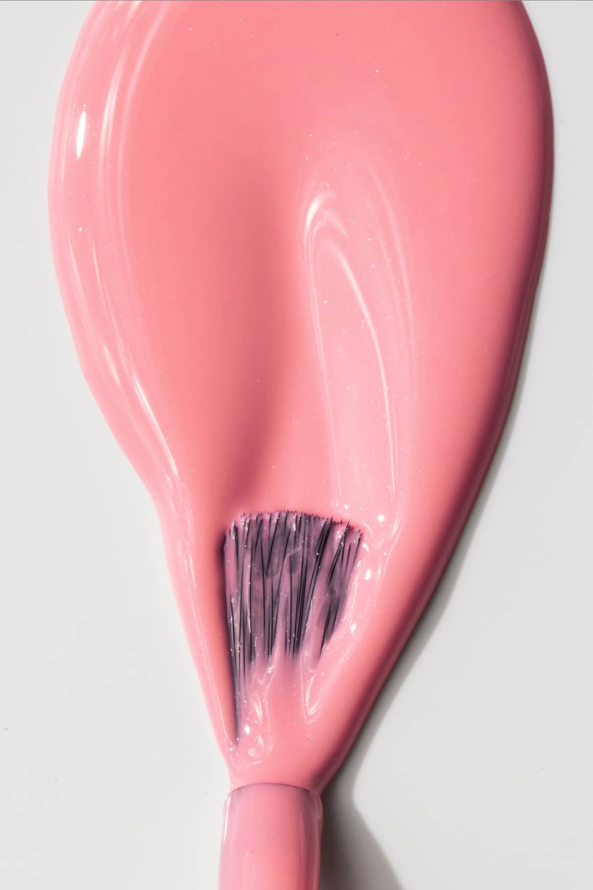 Nahaufnahme eines Nagellackpinsels, der mit gitti no. 007 beschichteten Pinsels, der auf einer weißen Fläche schwungvolle, glänzende rosa Striche erzeugt.