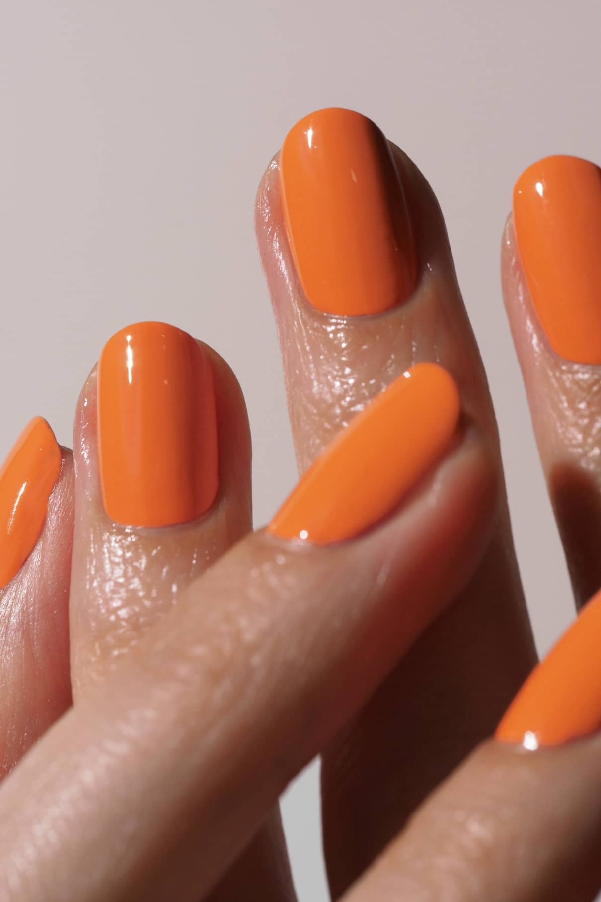 Nahaufnahme von sauber manikürten Nägeln, die mit gitti no. 008, einem glänzenden orangefarbenen Nagellack, vor einem einfarbigen Hintergrund.