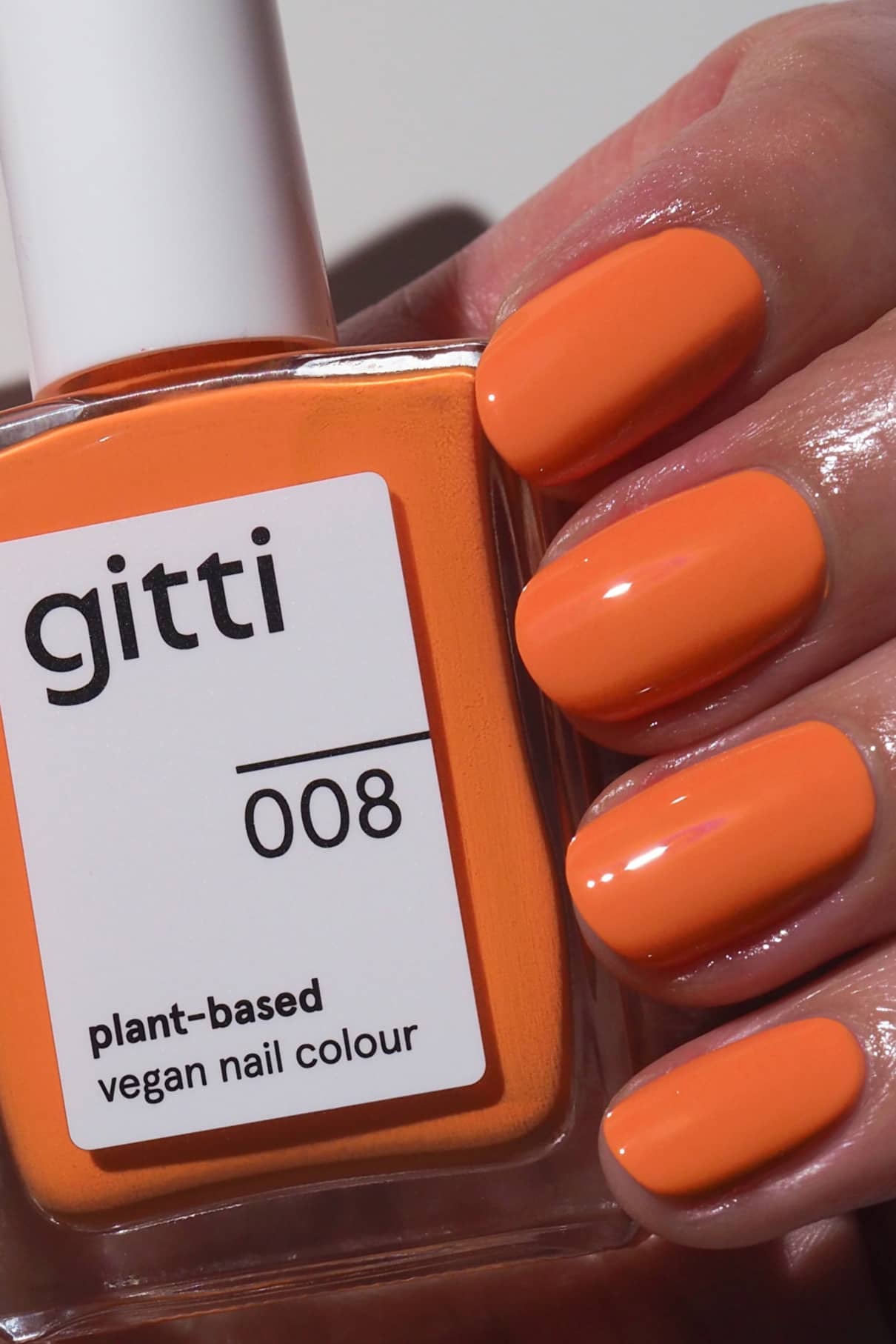 Eine Hand mit orange gefärbten Nägeln hält eine Flasche gitti no. 008, einer veganen Nagelfarbe auf Pflanzenbasis in einem leuchtenden Orangeton.