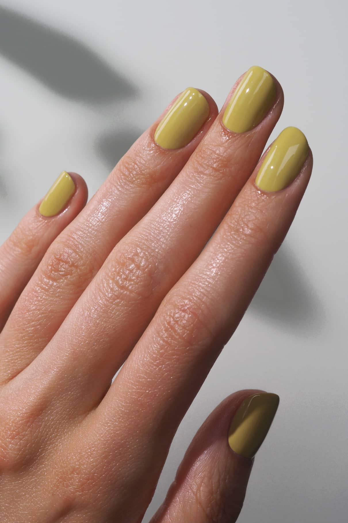 Eine Nahaufnahme einer Hand mit kurzen, sauber geformten Nägeln, die mit gitti no. 009, einem zarten pistaziengrünen Nagellack mit dezenten gelben Untertönen.