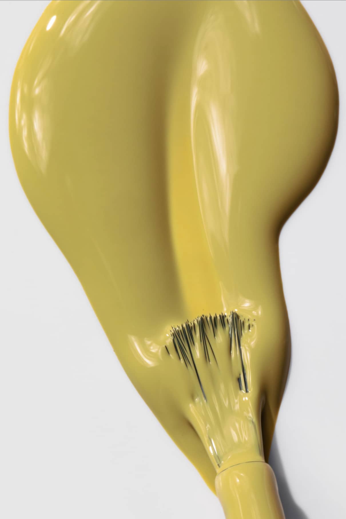 Ein Pinsel streicht gitti no. 009, ein gelber Farbton mit weichen, gelben Untertönen, in einem dicken Strich auf eine weiße Fläche.