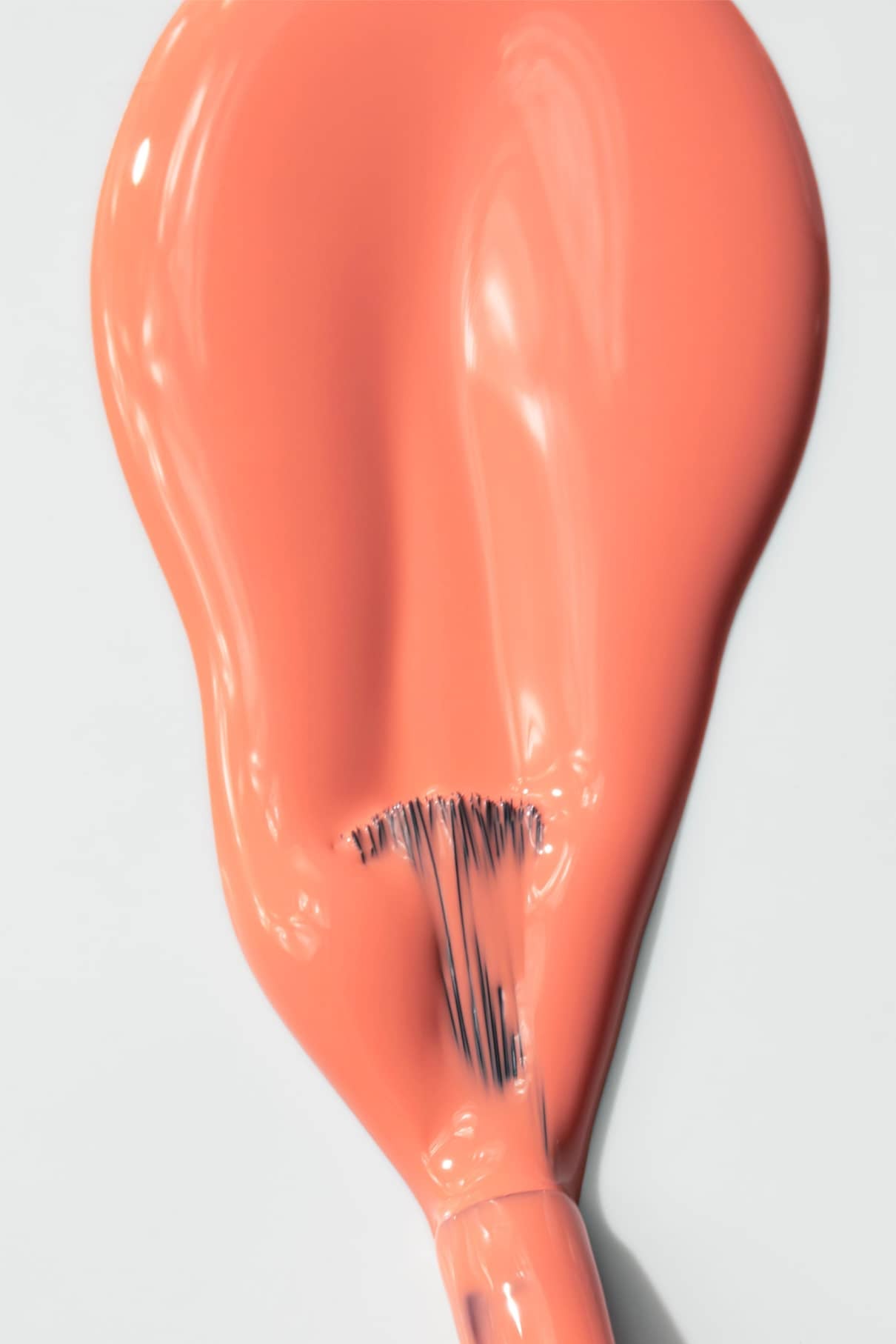 Nahaufnahme eines Pinsels, mit dem gitti no. 010 Nagellack in einem intensiven Korallenton auf. Er erzeugt einen glatten, glänzenden Strich auf einer weißen Oberfläche und hebt die elegante Farbnuance hervor.