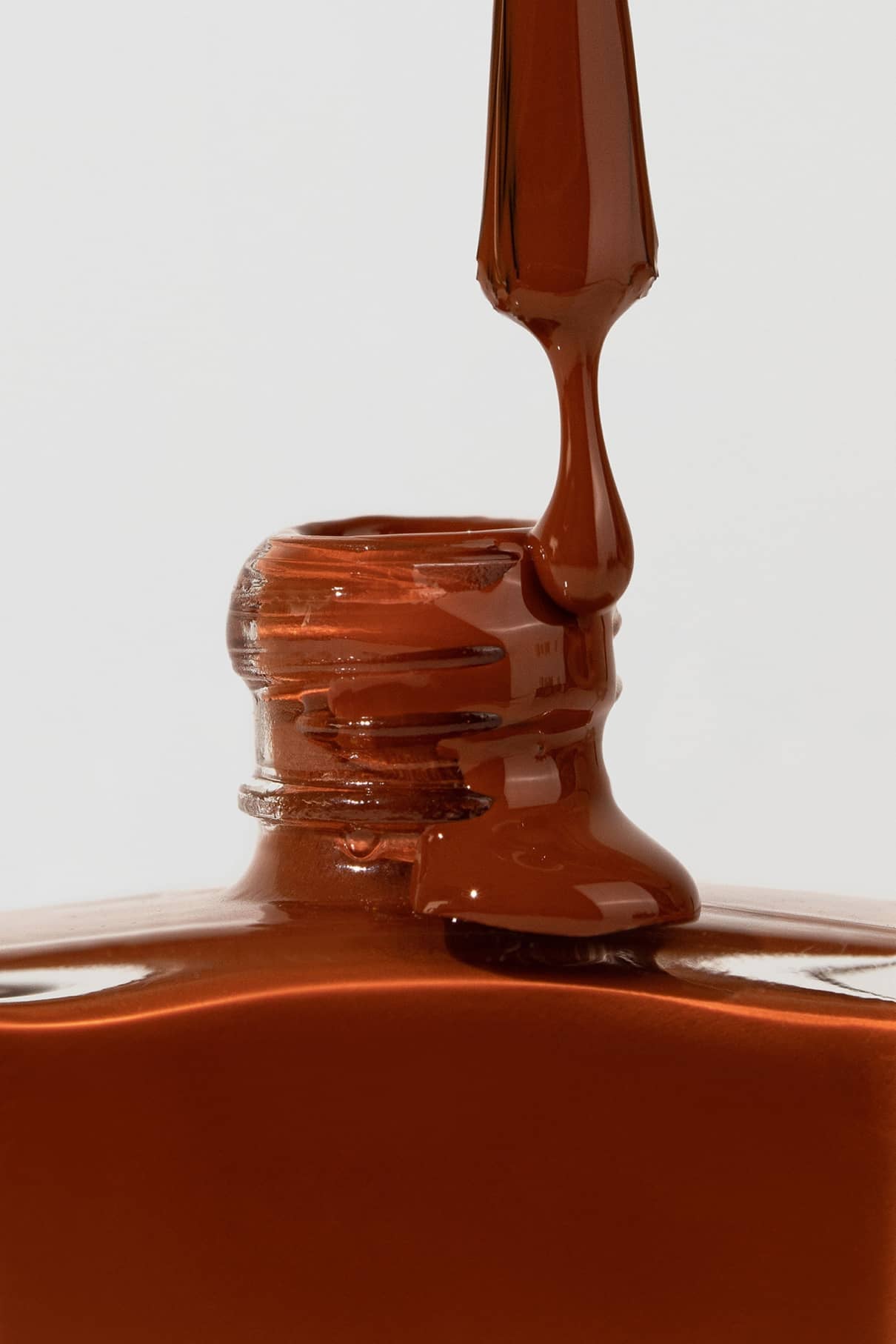 Eine Nahaufnahme eines Pinsels mit Gitti Nr. 014 Nagellack, der aus einer offenen Flasche gezogen wird, vor einem schlichten Hintergrund.