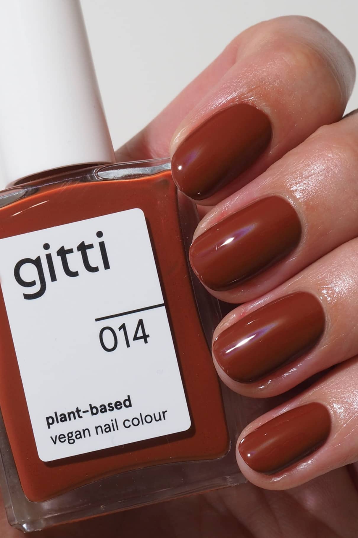 Eine Hand mit kurzen, sauber manikürten Nägeln, die in dem warmen, rötlich-braunen Farbton gitti no. 014 lackiert sind, hält eine Flasche mit pflanzlichem, veganem Nagellack.