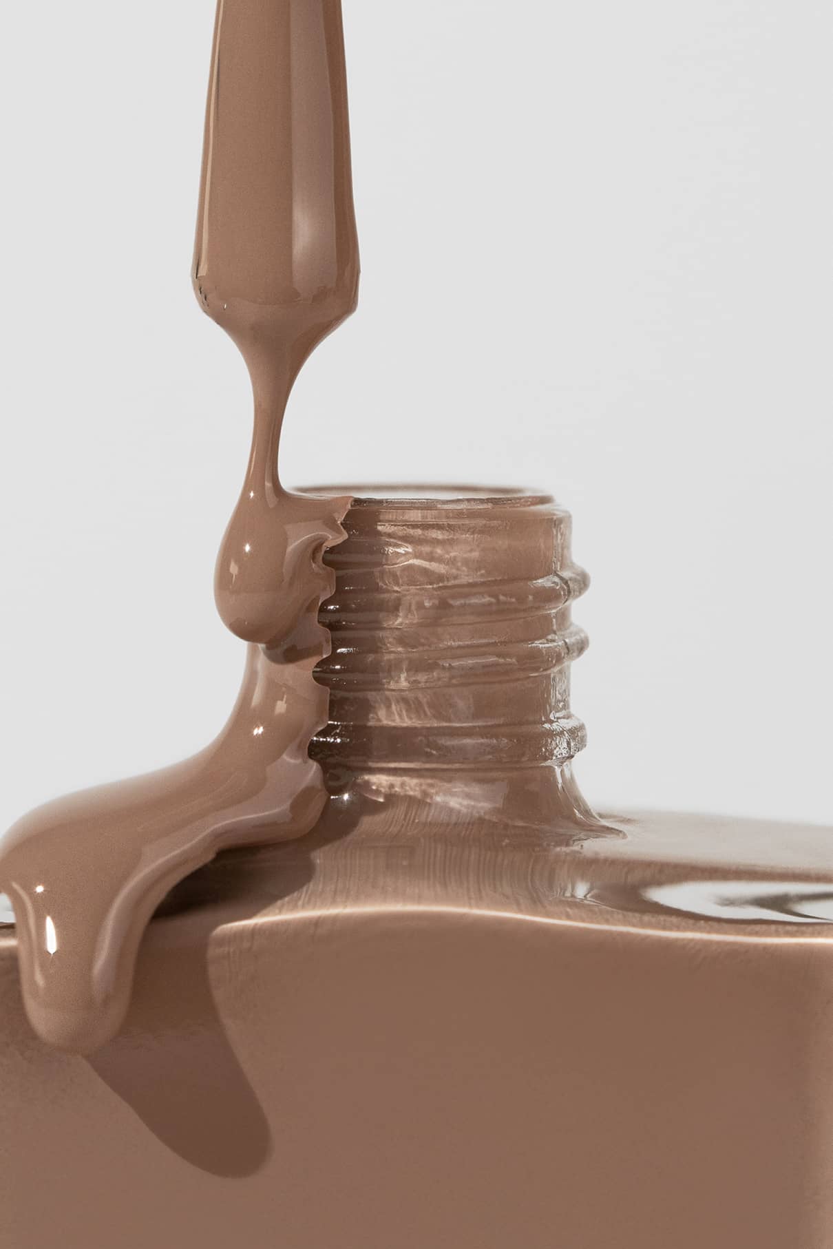 Eine Nahaufnahme eines Pinsels, der gitti no. 015, ein cremefarbener beiger Nagellack, auf den Hals einer offenen Flasche.