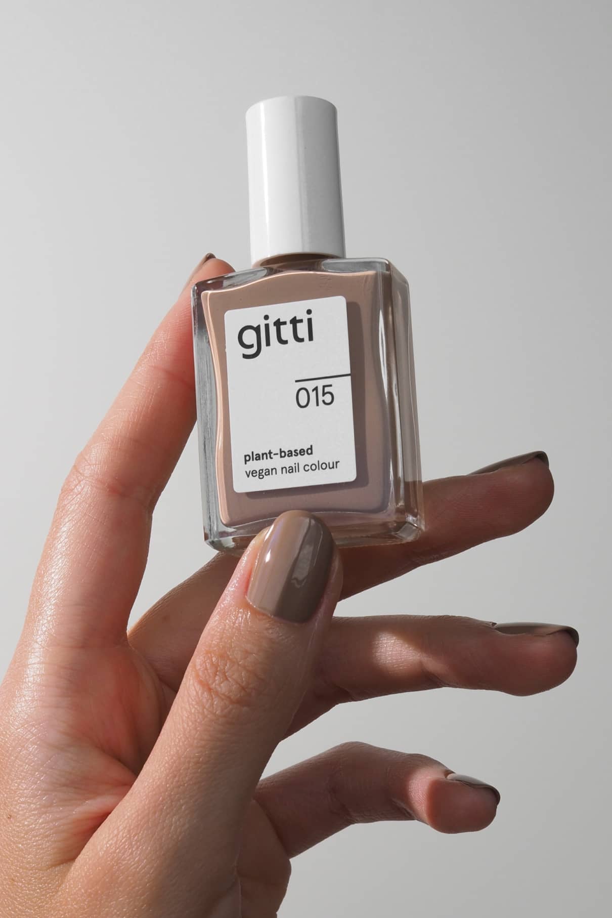 Eine Hand hält ein Fläschchen mit gitti no. 015; die Nägel sind in cremigem Beige lackiert, passend zum sanften Farbton der pflanzlichen veganen Nagelfarbe.