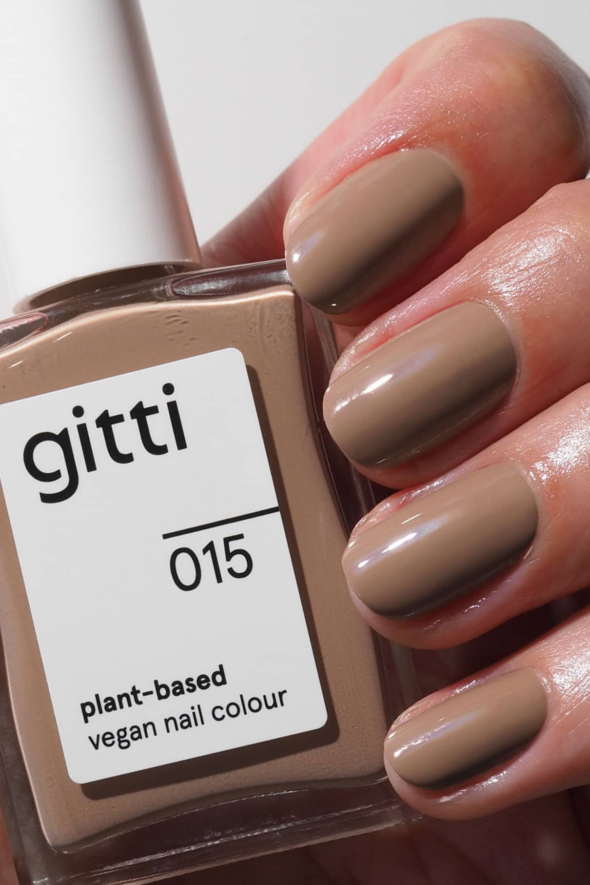 Eine Hand mit sauber manikürten, in cremigem Beige lackierten Nägeln hält eine Flasche gitti no. 015, einer pflanzlichen, veganen Nagelfarbe im selben Farbton.