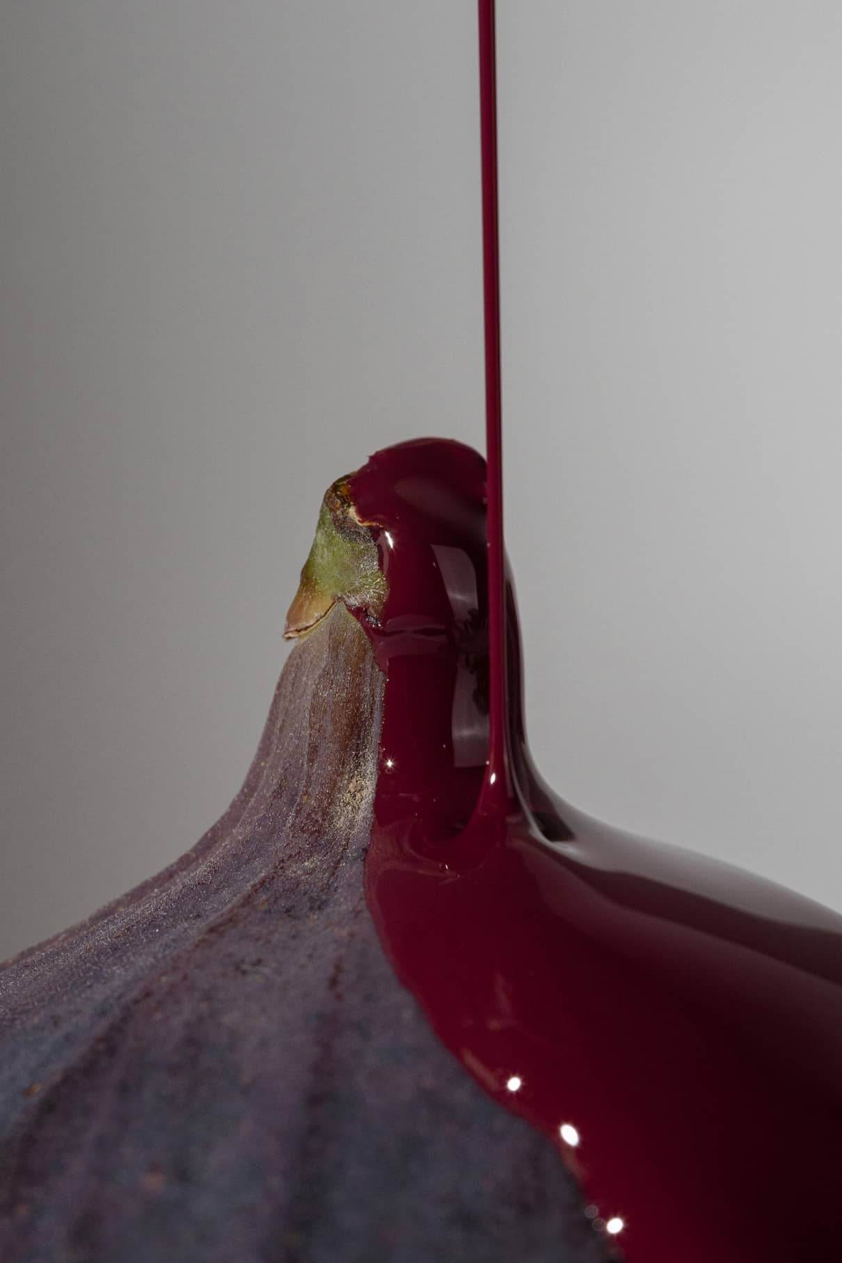 Nahaufnahme einer Feige, die mit einem Strahl von gitti no. 016, einem dicken, dunkelroten Lippenstift, vor einem schlichten hellen Hintergrund.