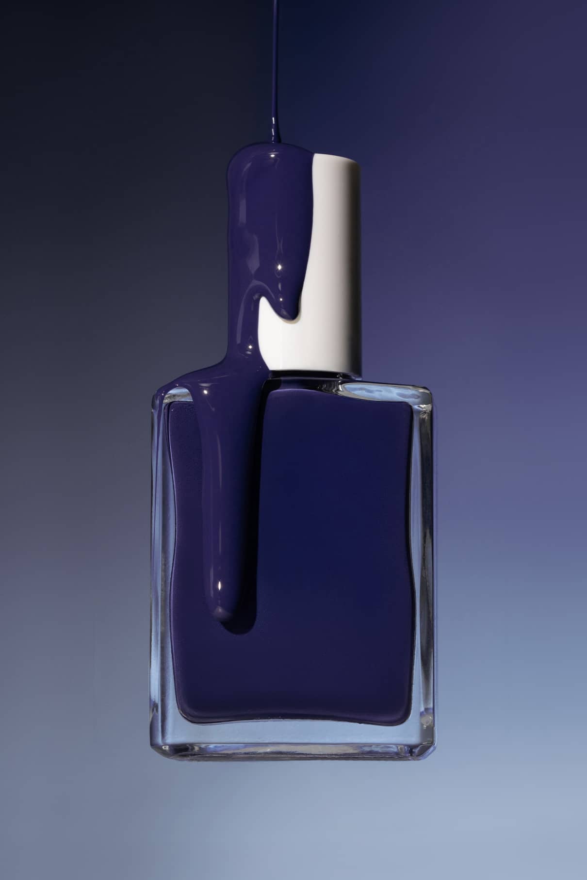 Eine Klarglasflasche mit silbernem Verschluss, teilweise gefüllt mit Gitti Nr. 018 - einer tiefblauen Politur - steht vor einem blauen Hintergrund mit Farbverlauf.