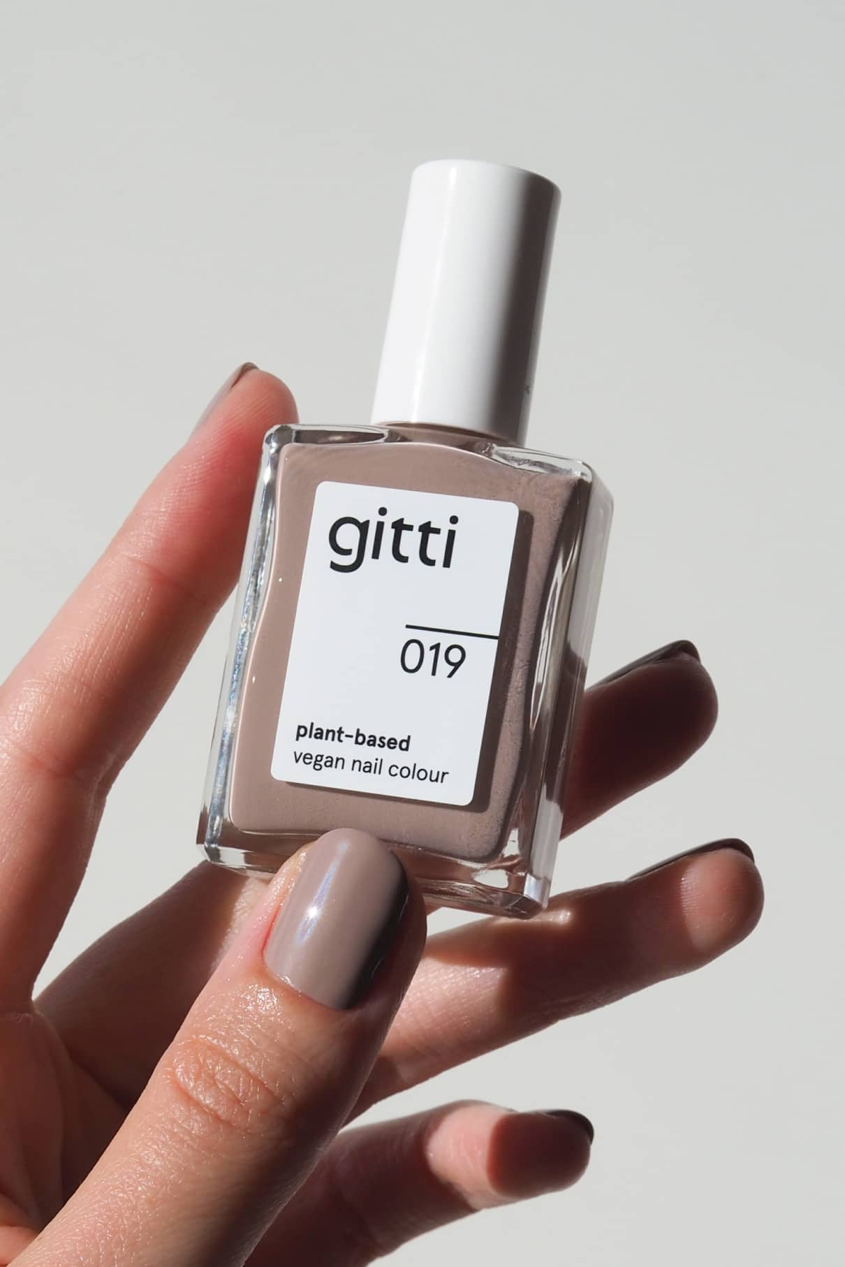 Eine Hand hält eine Flasche gitti no. 019 pflanzlicher veganer Nagellack. Die Nägel sind in demselben zarten Mauve-Ton mit beigen Untertönen lackiert.