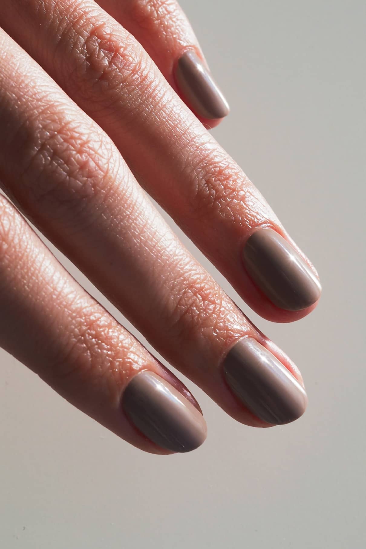 Nahaufnahme einer Hand mit kurzen, sauber manikürten Nägeln, die in dem glänzenden Taupe-Ton "gitti no. 019" mit zarten mauvefarbenen und beigen Untertönen.