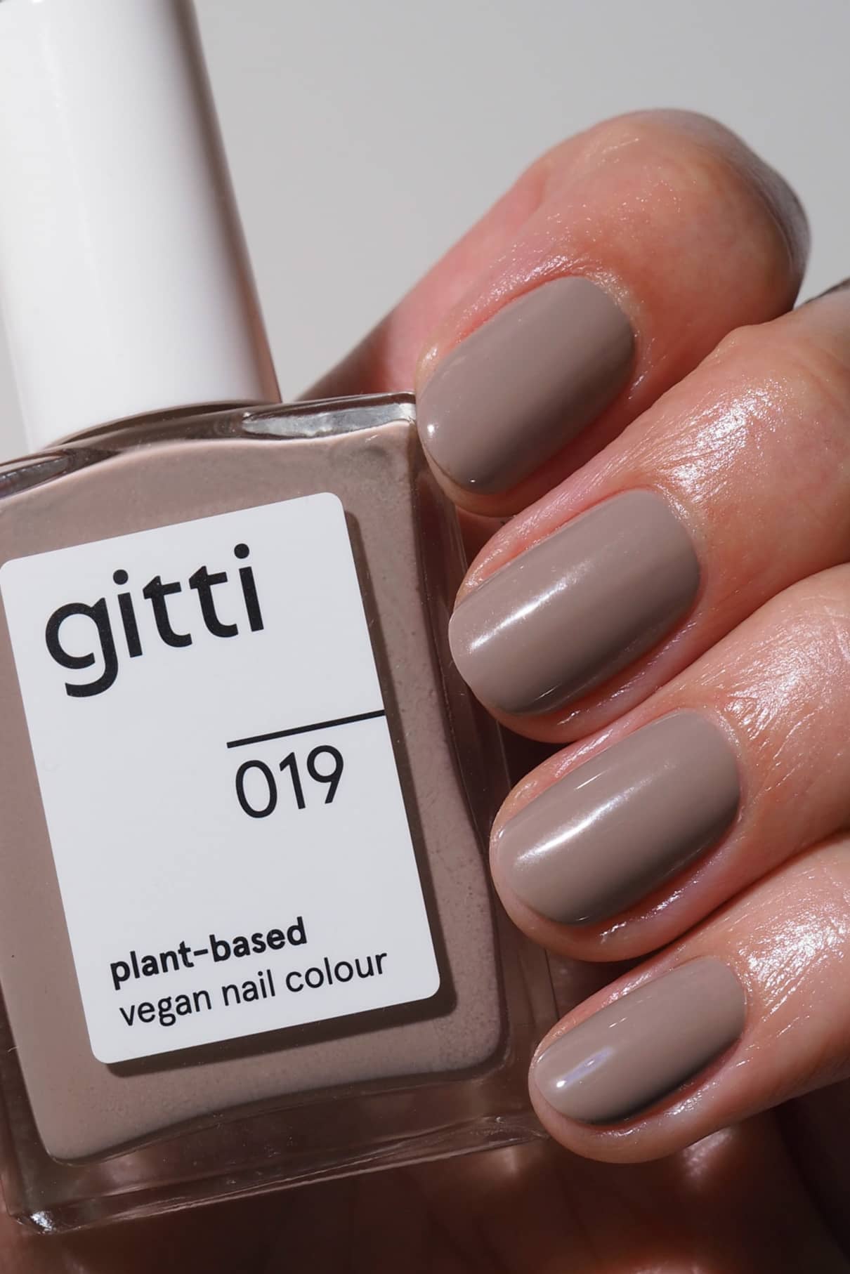 Eine Hand mit sauber manikürten, in zartem Mauve lackierten Nägeln, die eine Flasche gitti no. 019 pflanzlicher veganer Nagellack in einem passenden Farbton mit beigen Untertönen.