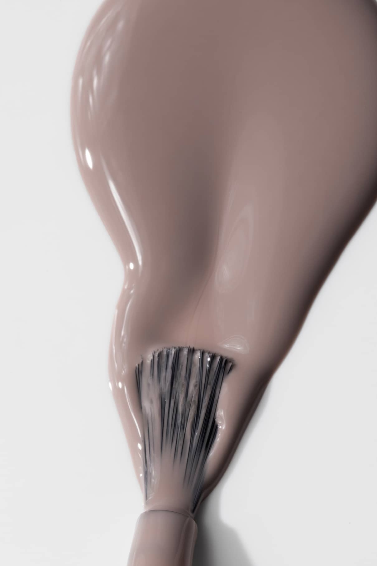 Nahaufnahme eines Pinsels, der eine dicke Schicht von gitti no. 019, einem taupefarbenen Nagellack mit zarten mauvefarbenen und beigen Untertönen, auf eine weiße Fläche auf.