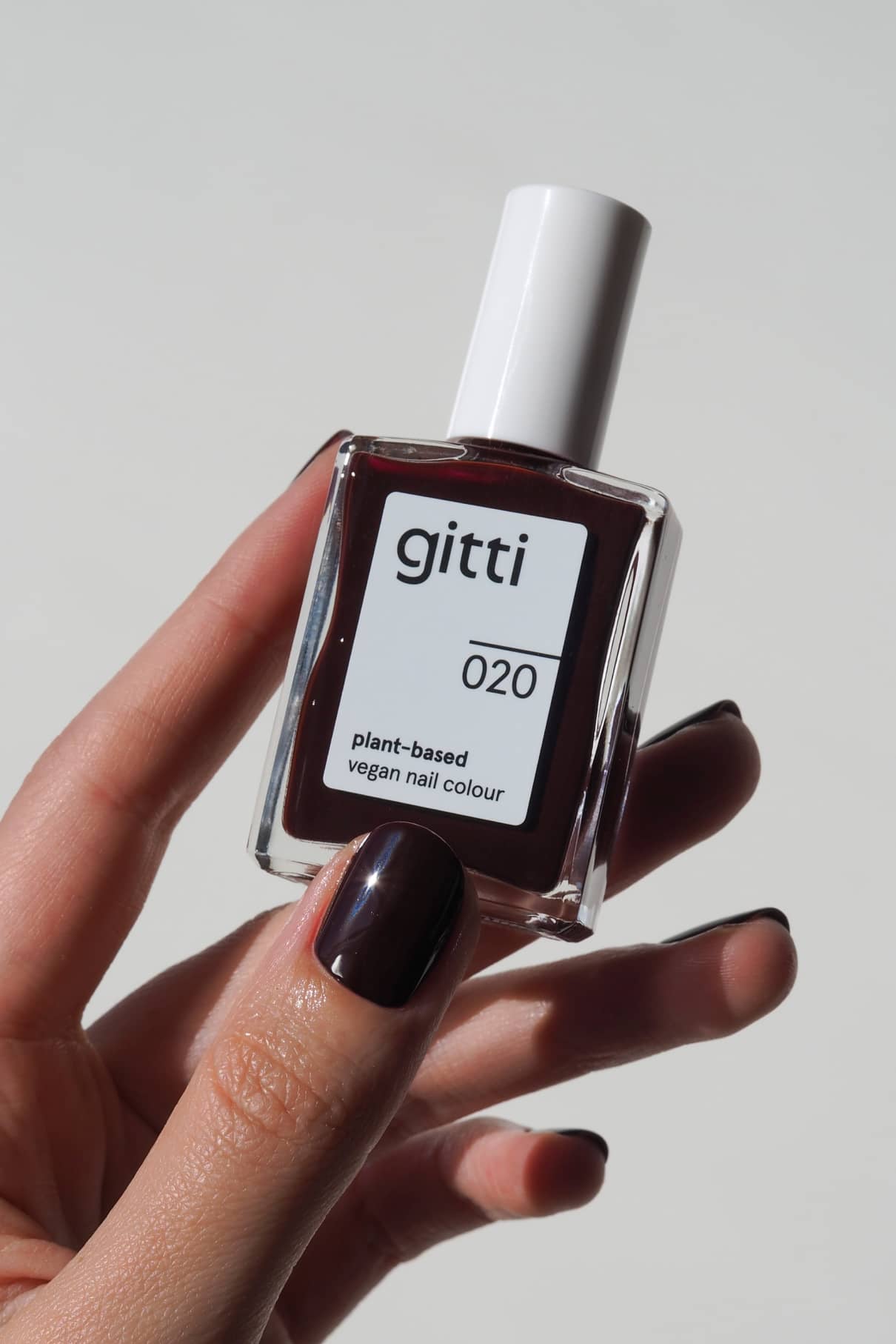 Eine Hand hält eine Flasche mit gitti no. 020 pflanzlicher veganer Nagelfarbe; die Nägel sind in einem passenden, intensiven Rotton lackiert.