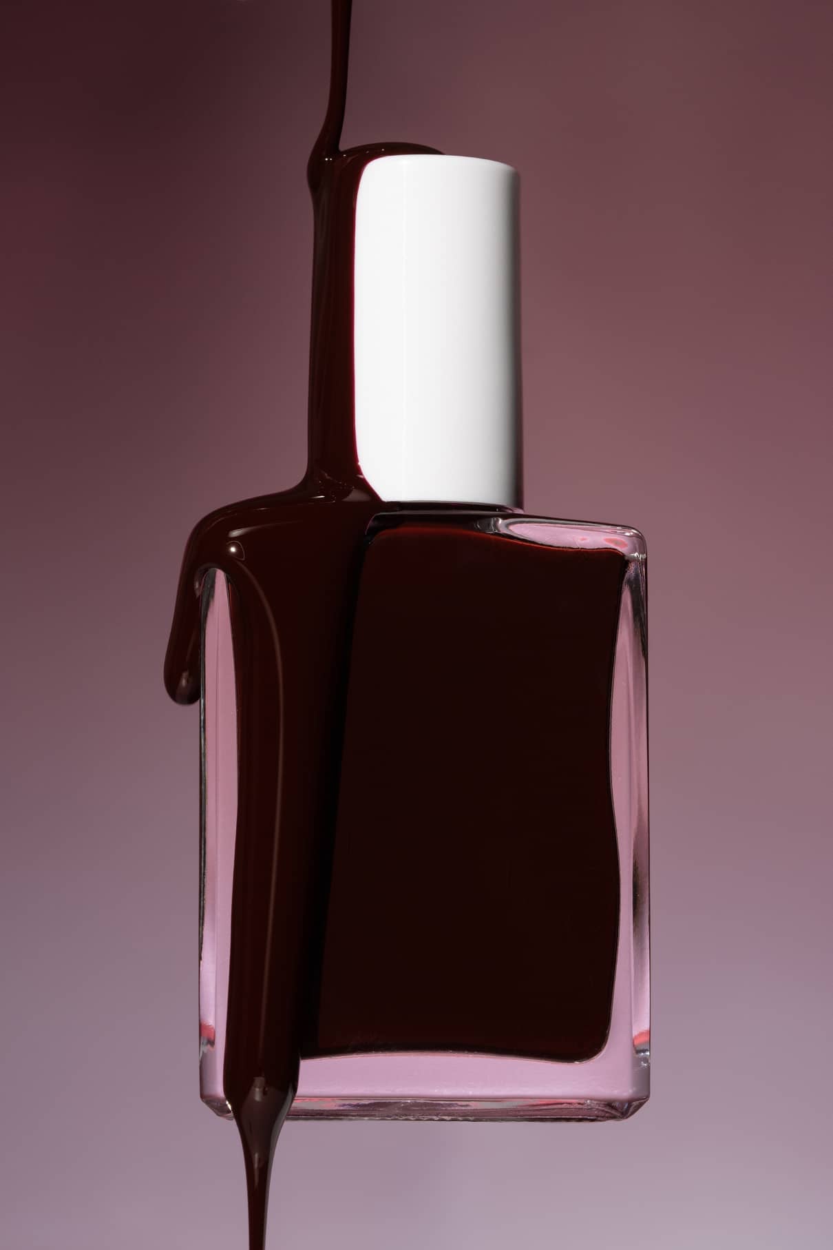Eine klare Glasflasche von gitti no. 020 mit weißer Kappe ist teilweise von leuchtend rotem Nagellack bedeckt, der auf einen rosa Hintergrund mit Farbverlauf tropft.