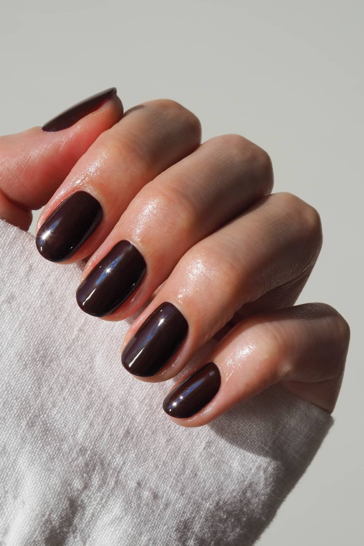 Eine Hand mit kurzen, sauber manikürten Nägeln, lackiert in dem glänzenden Rotton von gitti no. 020, teilweise verdeckt durch einen weißen Ärmel.