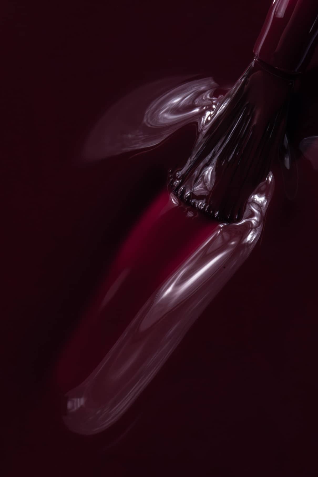 Nahaufnahme eines Nagellackpinsels, mit dem gitti no. 020, ein glänzender, tiefroter Farbton, auf einen Fingernagel auf, wobei seine reichhaltige und flüssige Textur hervorgehoben wird.