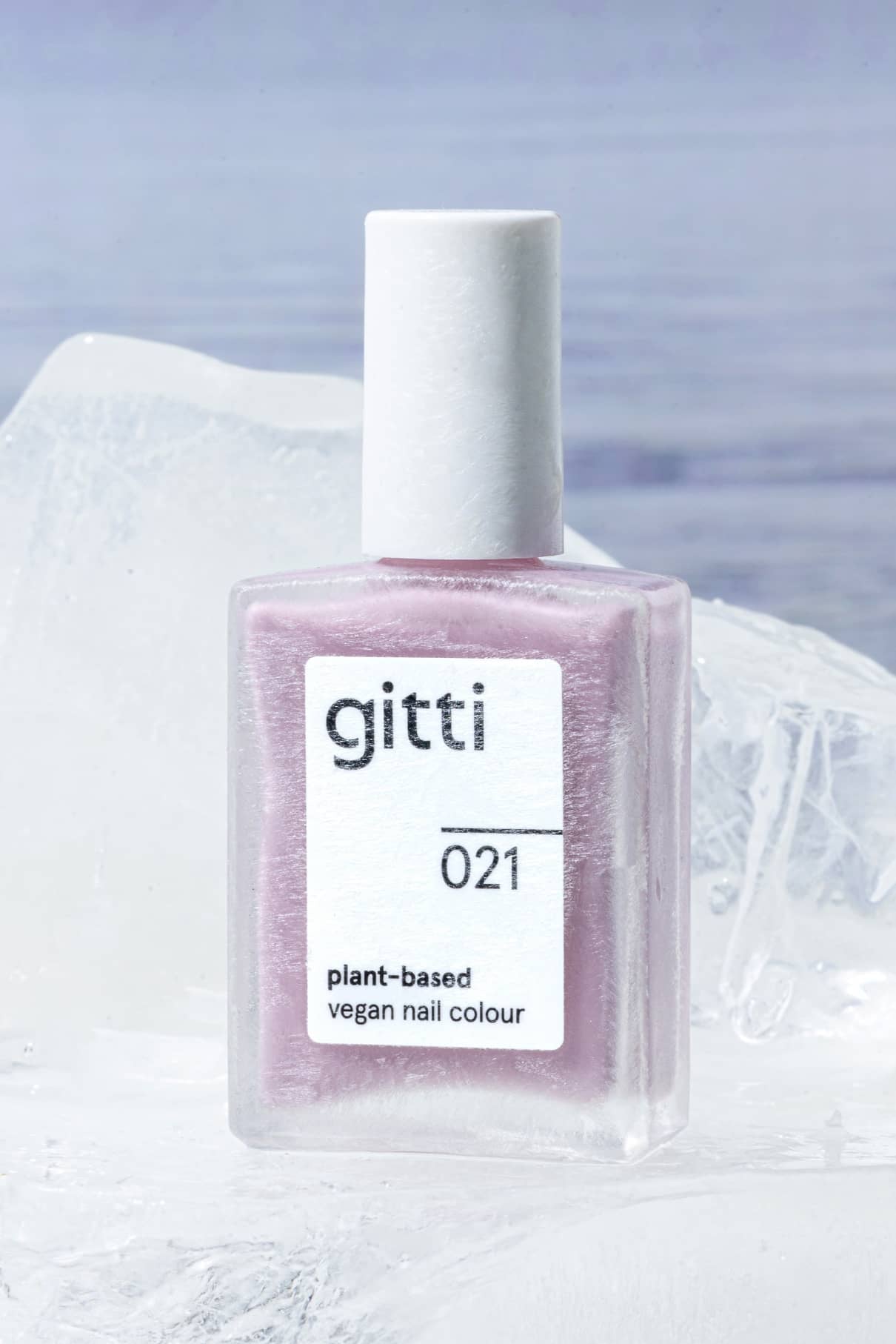 Eine Flasche von gitti no. 021 pflanzlicher veganer Nagellack in einer gefrosteten rechteckigen Flasche ruht auf einem großen Eisblock vor einem weichen, pudrigen lilafarbenen Hintergrund.