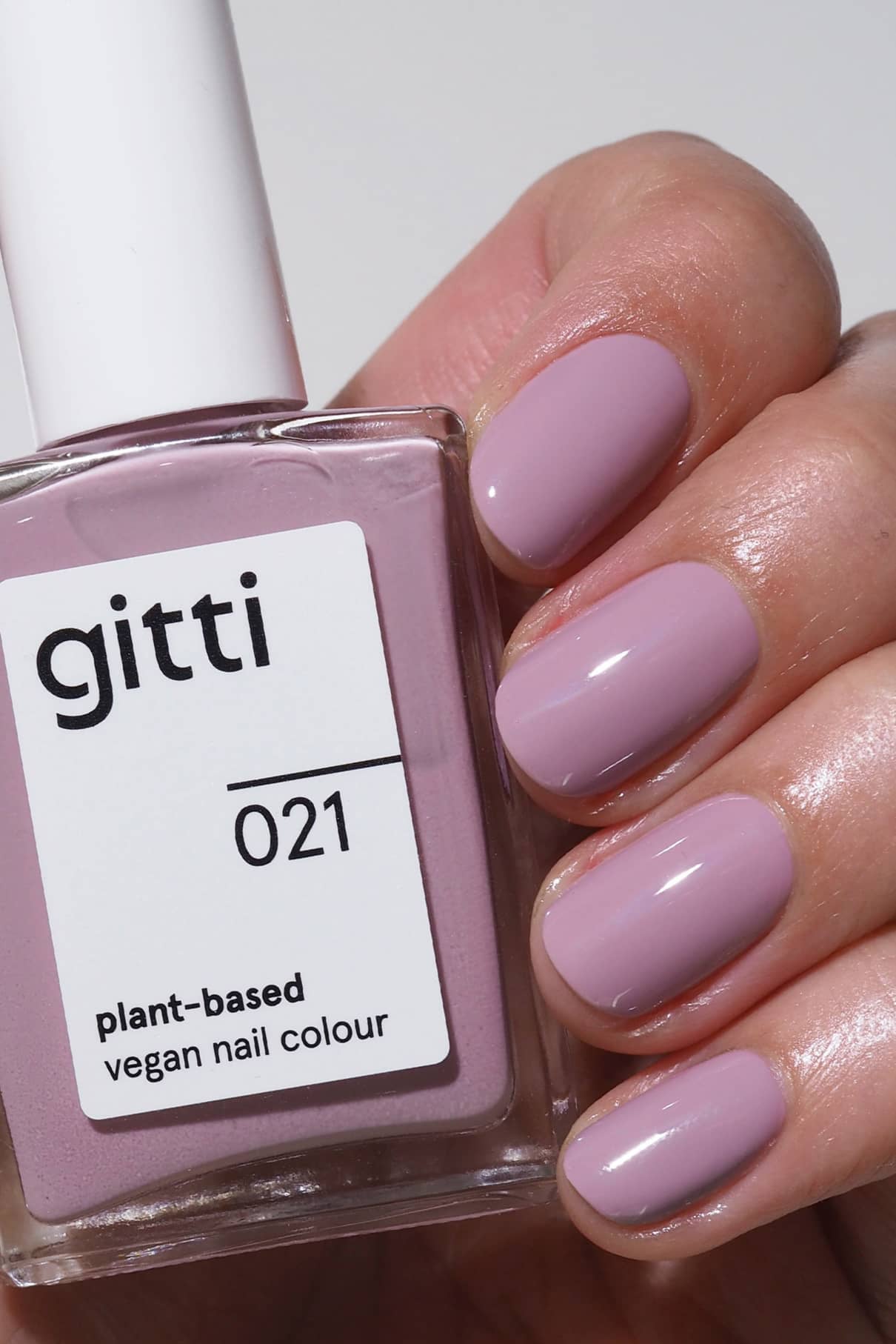 Eine Hand mit sauber manikürten Nägeln in pudrigem Lila hält eine Flasche gitti no. 021, einem pflanzlichen veganen Nagellack im gleichen Farbton.