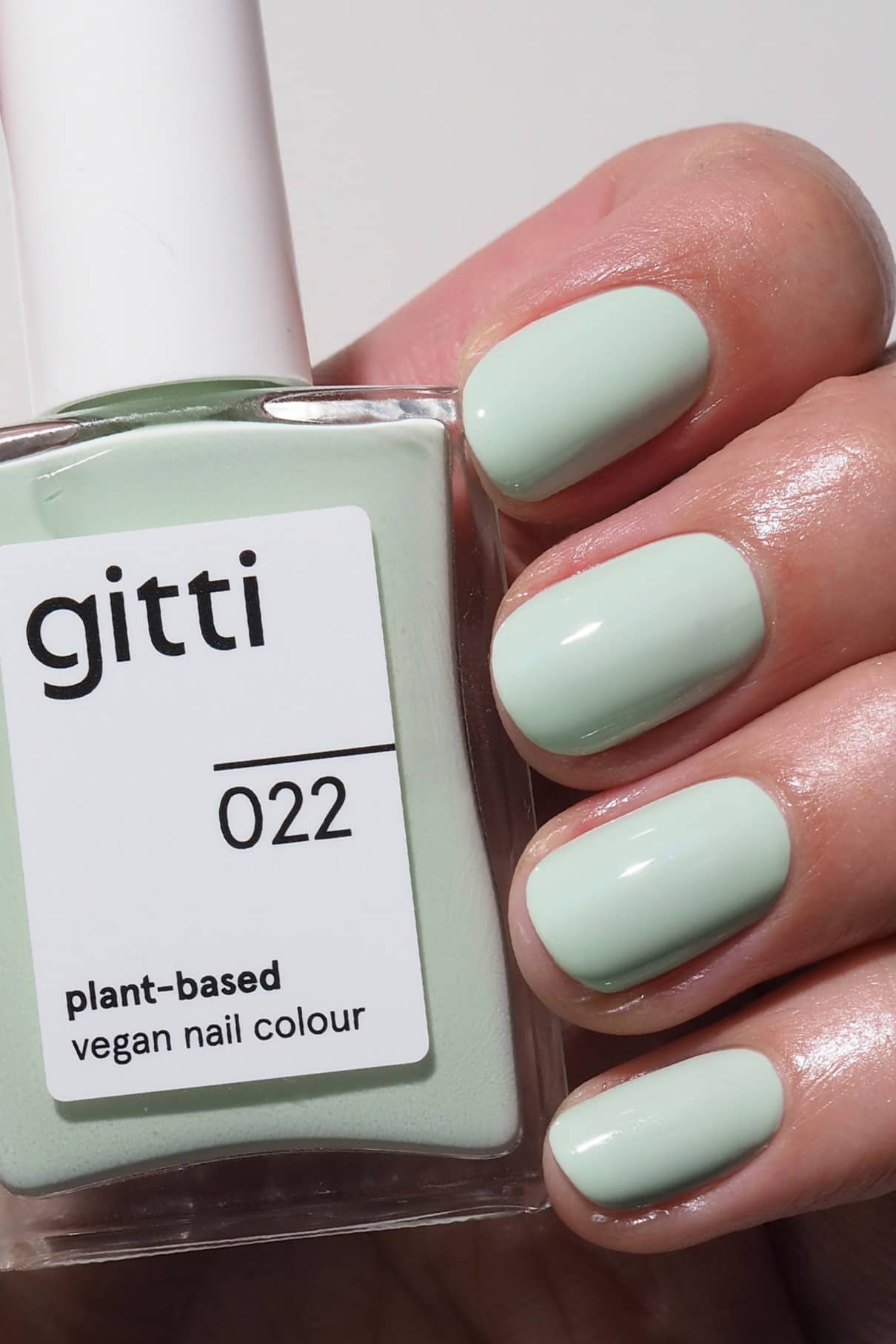 Eine Hand mit sauber manikürten, in frischem Minzgrün lackierten Nägeln hält eine Flasche gitti no. 022, einer veganen Nagelfarbe auf Pflanzenbasis.