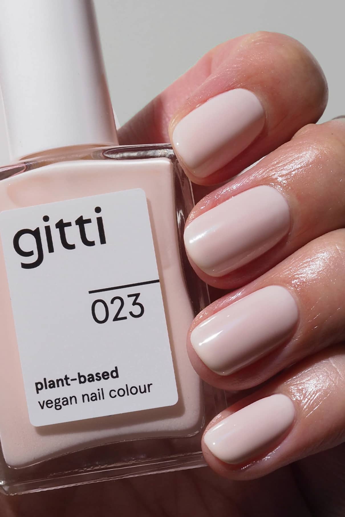 Eine Hand mit kurzen, sauber manikürten Nägeln in einem milchigen Rosé-Ton hält eine Flasche gitti no. 023 veganen Nagellack auf Pflanzenbasis.