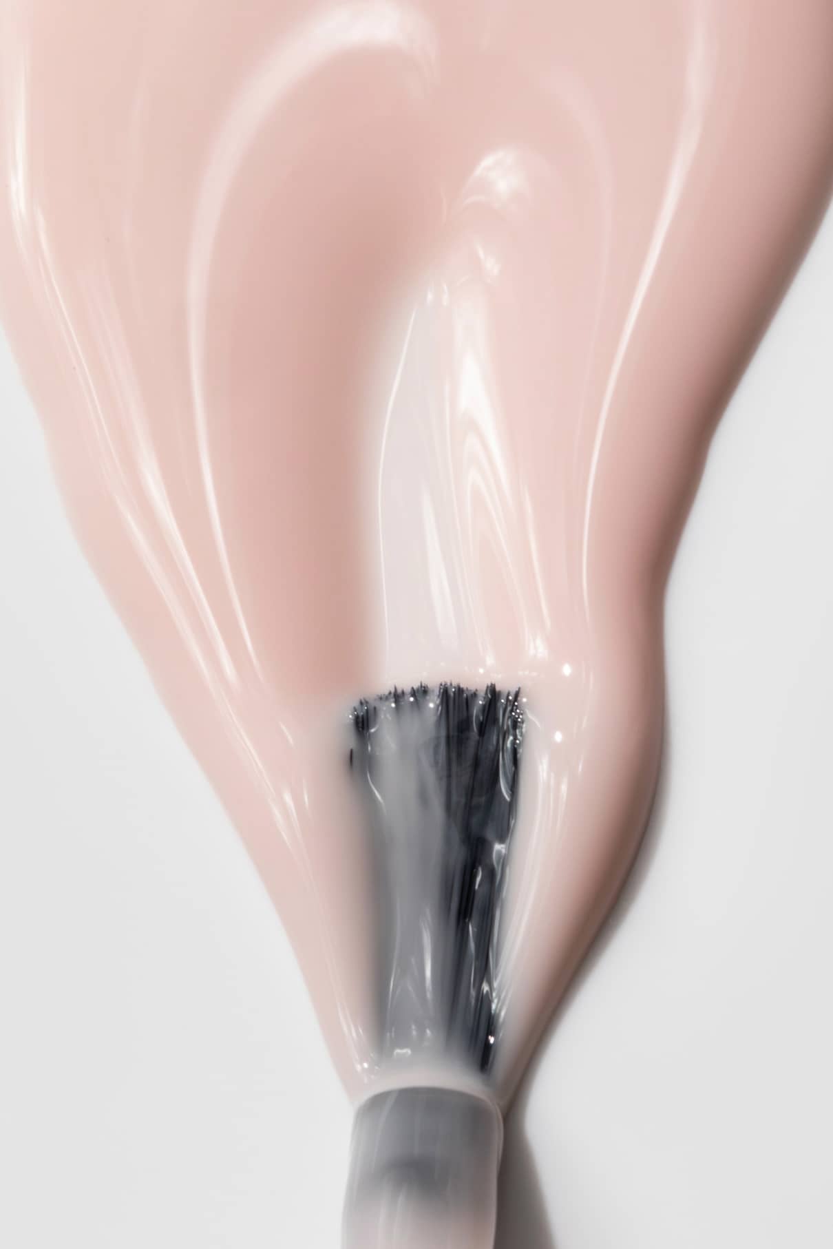 Nahaufnahme eines Nagellackpinsels, mit dem gitti no. 023, einen milchigen Rosé-Ton, auf eine glatte weiße Oberfläche aufzutragen.