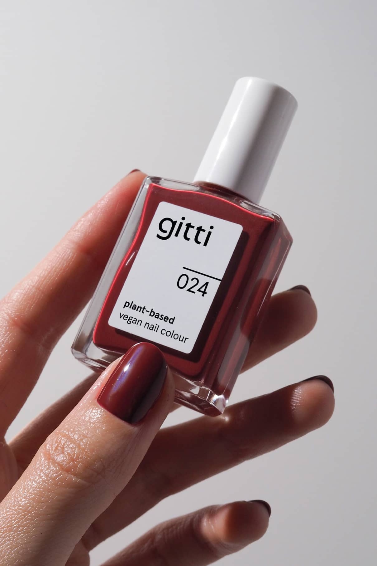 Eine Hand mit rot lackierten Nägeln hält eine Flasche von gitti no. 024, einer pflanzlichen, veganen Nagelfarbe in Dunkles Rot.