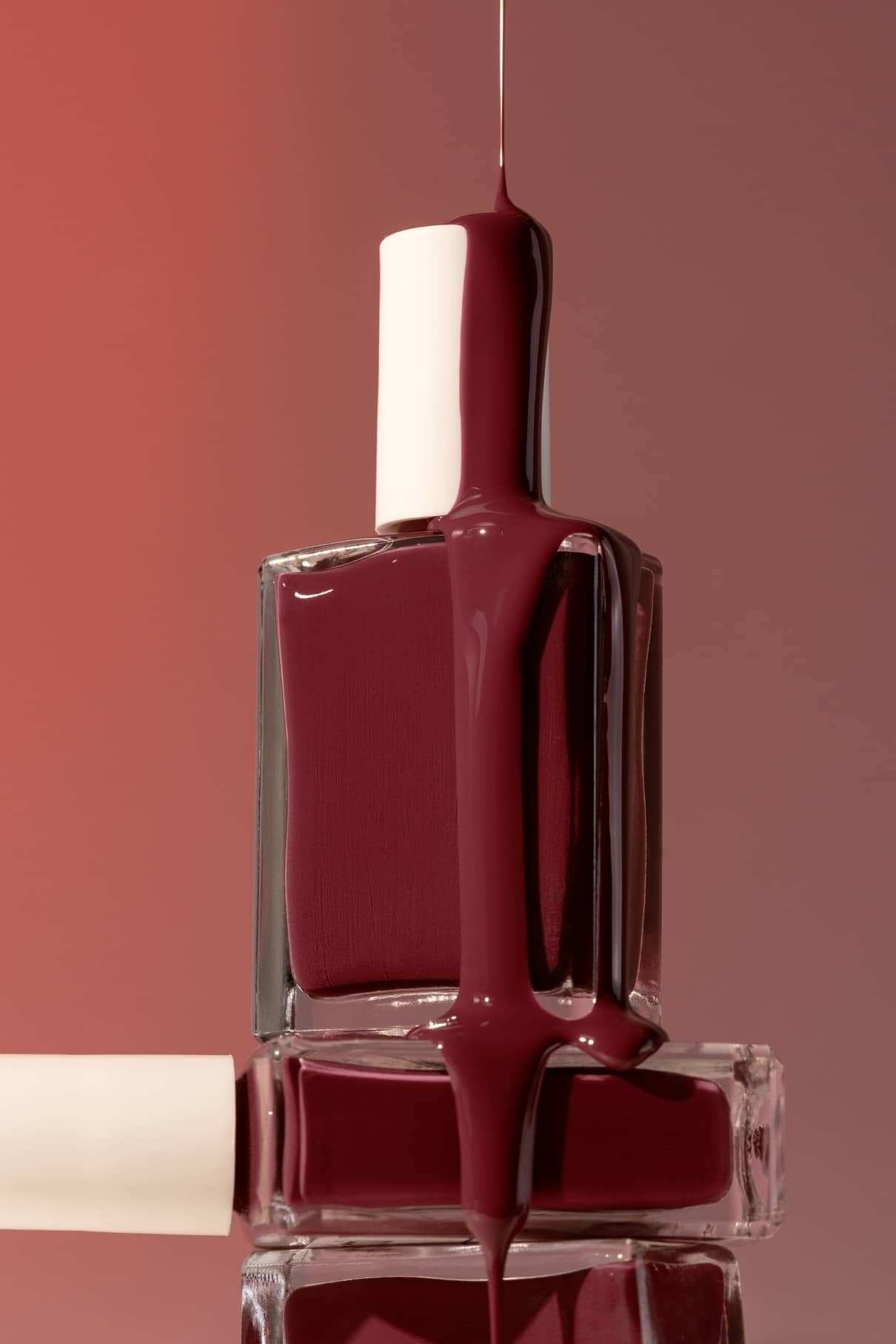Eine Flasche gitti no. 024 Nagellack steht auf einer anderen, wobei der leuchtende dunkelrote Farbton überläuft und an den Seiten heruntertropft.