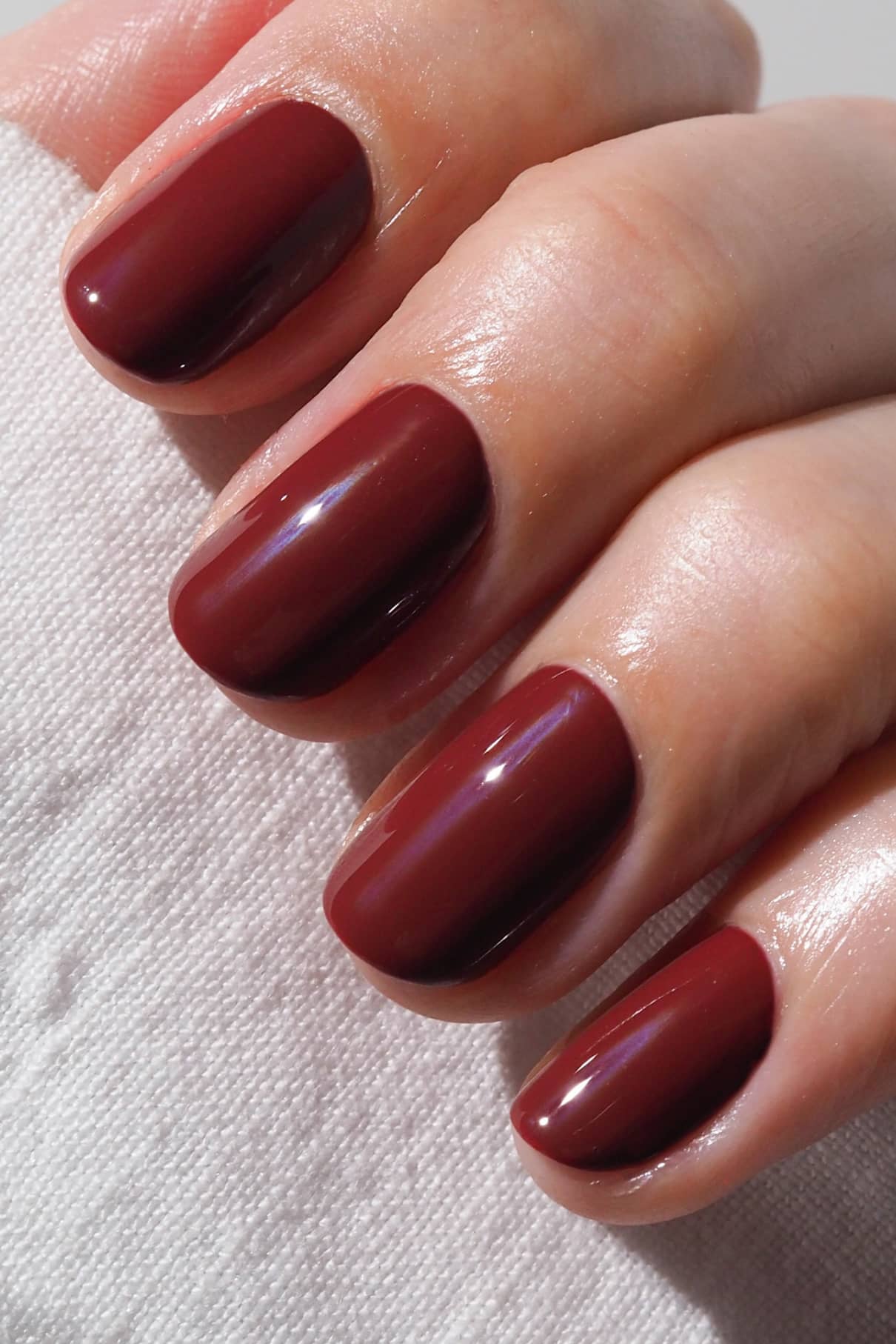 Nahaufnahme einer Hand mit sauber manikürten Nägeln, die in der glänzenden Farbe gitti no. 024, die auf einem strukturierten weißen Stoff ruht.