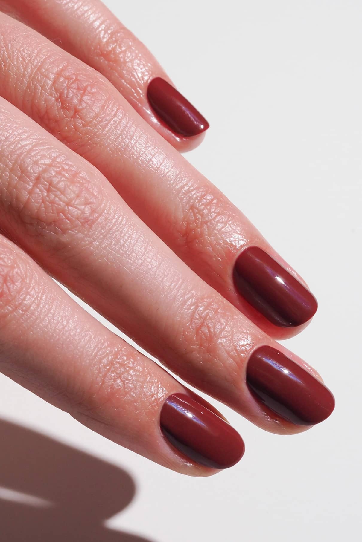 Eine Hand mit sauber manikürten Nägeln, lackiert mit glänzendem gitti no. 024 darkles Rot lackiert sind, ruht auf einer weißen Fläche.