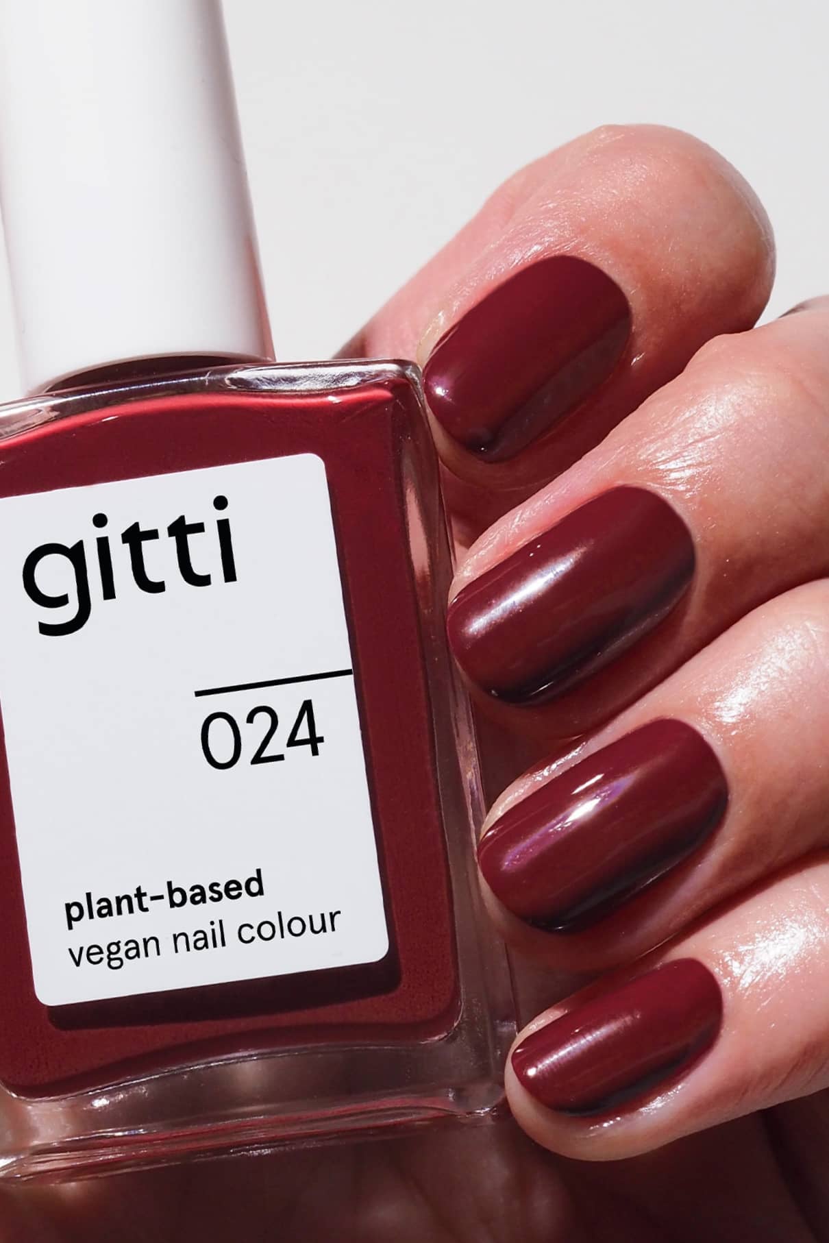 Eine Hand mit kurzen, sauber manikürten und tiefrot lackierten Nägeln hält ein Fläschchen mit gitti no. 024, einem veganen Nagellack auf Pflanzenbasis.