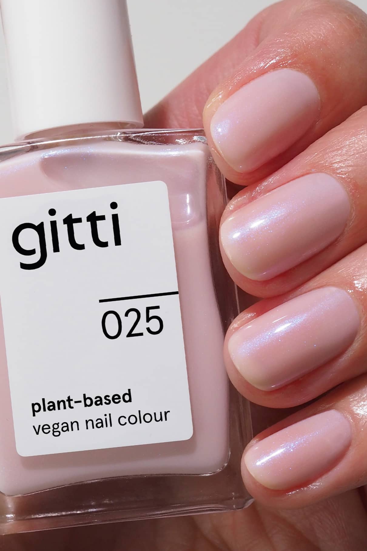 Eine Hand mit glänzenden, blassrosa Nägeln hält ein Fläschchen aus der Quick Dry Routine, einem pflanzlichen, veganen Nagellackset in einem passenden Farbton, das mit dem High Gloss Top Coat für zusätzlichen Glanz abgeschlossen wird.