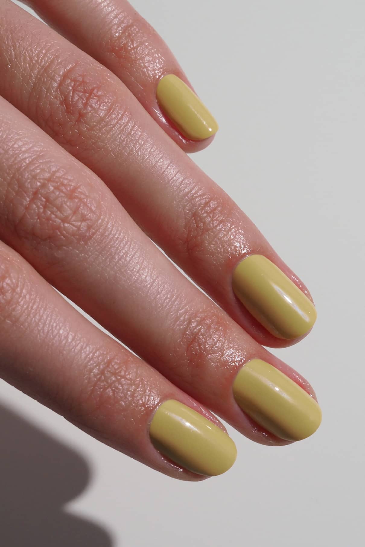 Eine Nahaufnahme einer Hand mit kurzen, sauber manikürten Nägeln, die mit gitti no. 026, einem glänzenden pastellgelben Lack mit dezentem grünem Touch.
