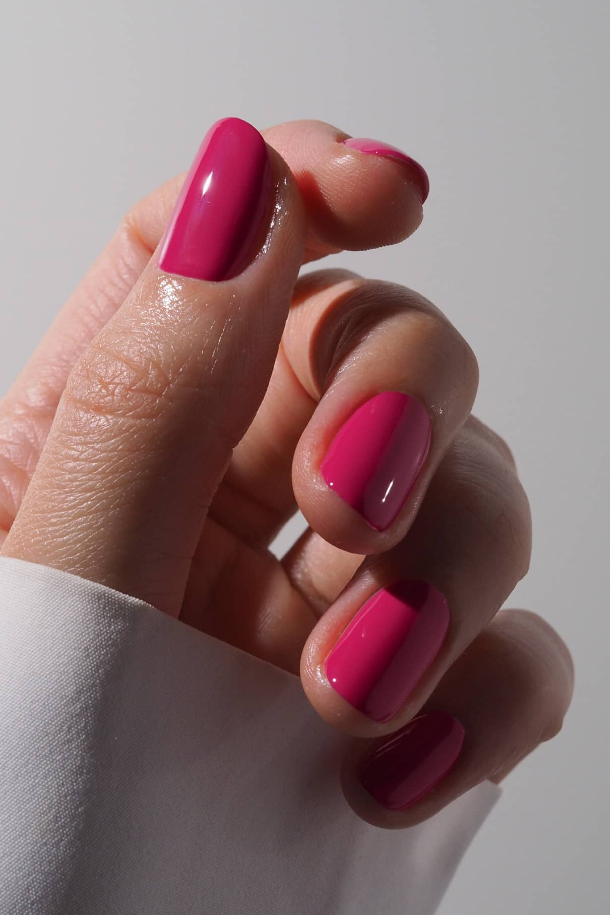 Nahaufnahme einer Hand mit kurzen, sauber manikürten Nägeln, die mit gitti no. 027, einem leuchtenden fuchsia-pinkfarbenen Lack, vor einem neutralen Hintergrund.