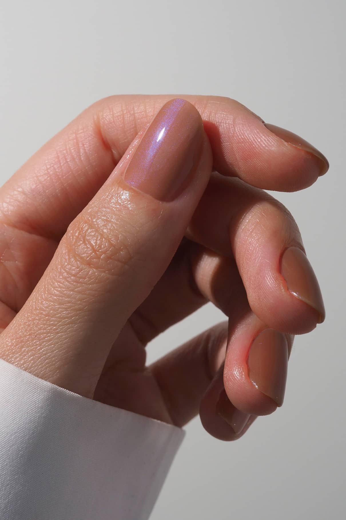 Nahaufnahme einer Hand mit sauber manikürten Nägeln, lackiert mit gitti no. 028, einem warmen, nudefarbenen, glänzenden Lack mit dezentem blauen Schimmer, vor einem schlichten, hellen Hintergrund.