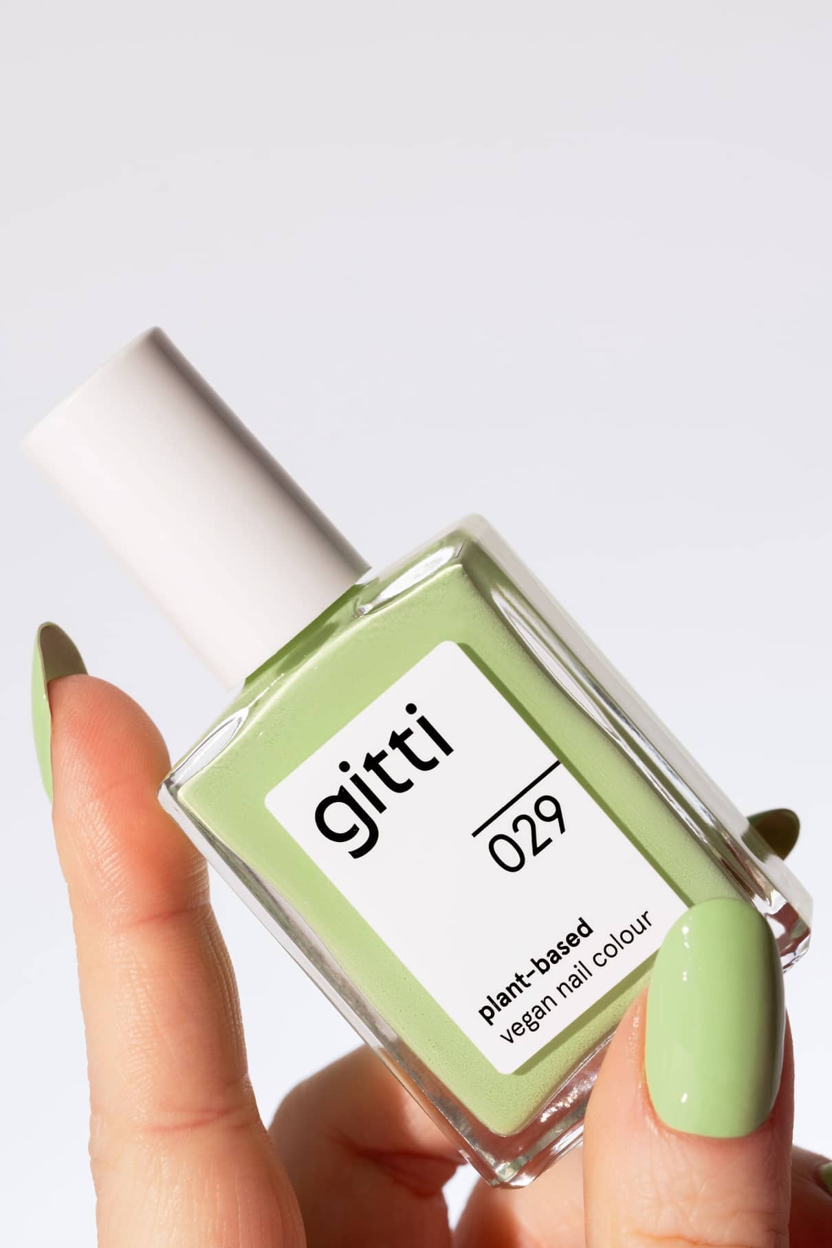 Eine Hand mit grün lackierten Nägeln hält eine Flasche von gitti no. 029, einer pflanzlichen, veganen Nagelfarbe in Pastellgrün - einem frischen, belebenden hellgrünen Farbton.