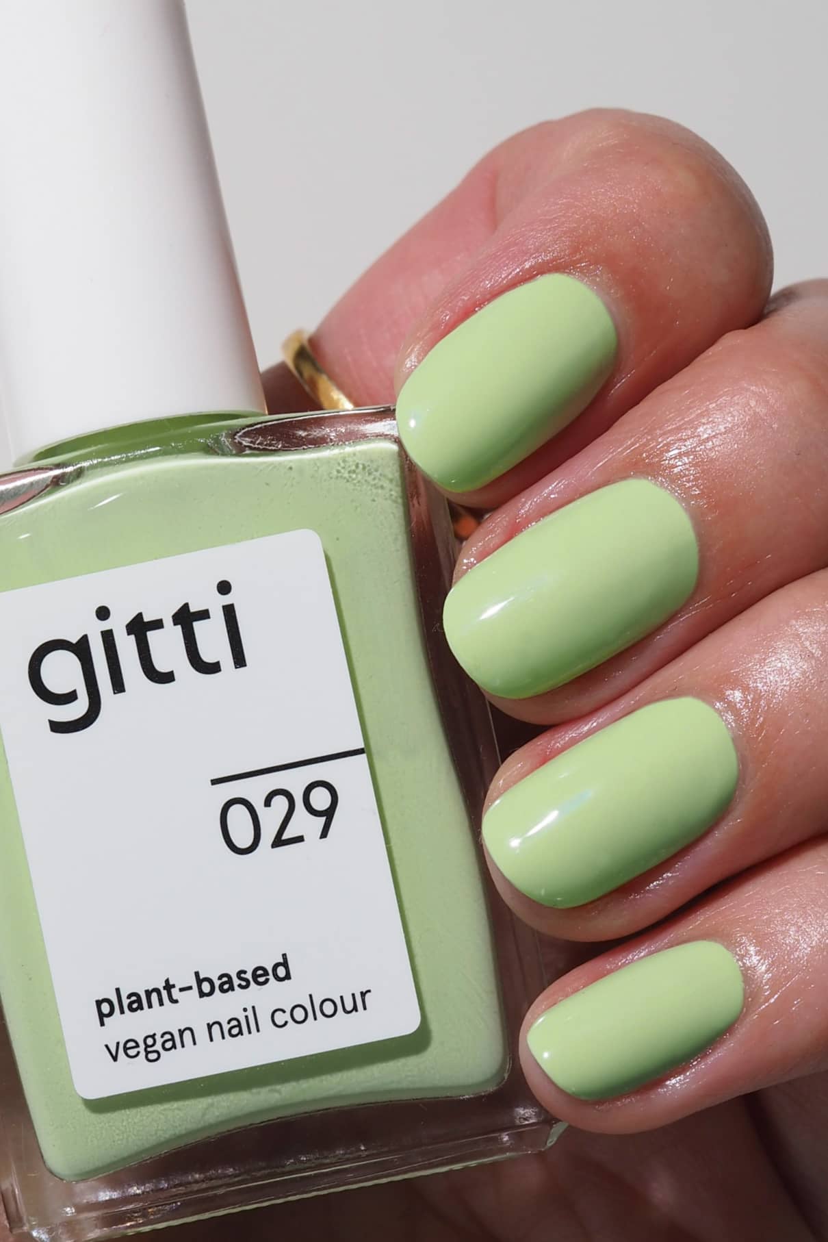 Eine Hand mit kurzen, in frischem, pastellfarbenem belebendem Grün lackierten Nägeln hält eine Flasche gitti no. 029 pflanzlichen veganen Nagellack im passenden Farbton.
