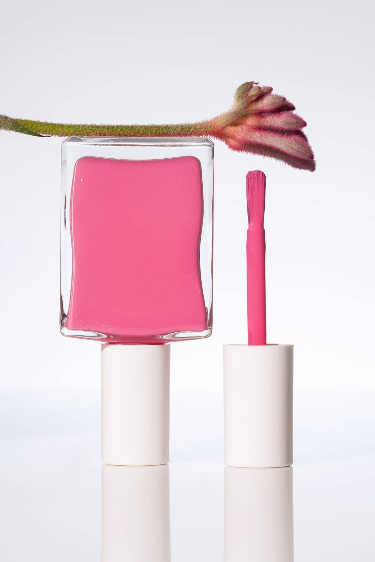 Eine Flasche gitti no. 030 Nagellack mit Pinsel und Kappe daneben, neben einer rosafarbenen Blumenknospe auf einem schlichten weißen Hintergrund.