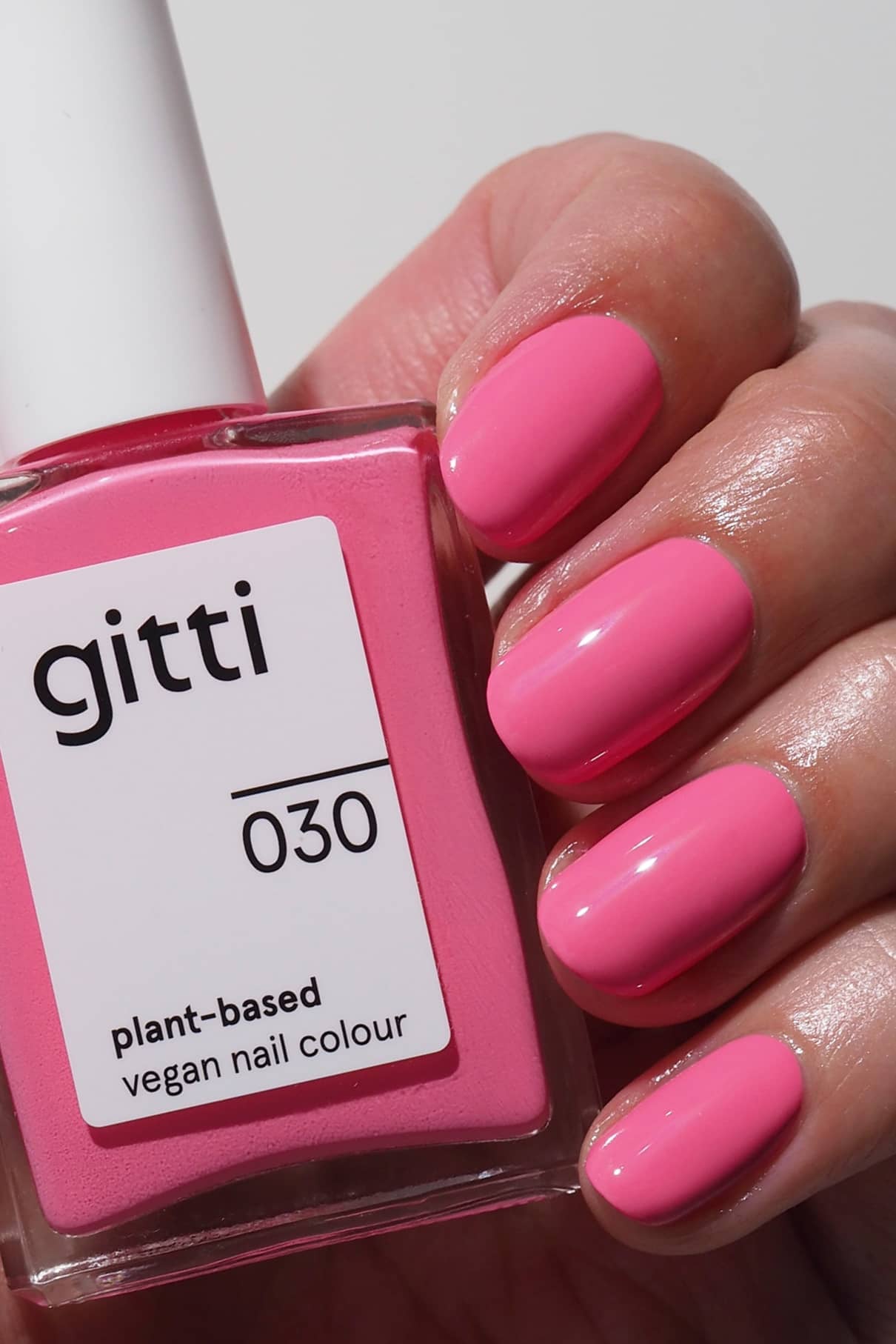 Eine Hand mit sauber manikürten, in leuchtendem Pink lackierten Nägeln hält eine Flasche gitti no. 030 pflanzliche vegane Nagelfarbe in einem passenden Farbton.