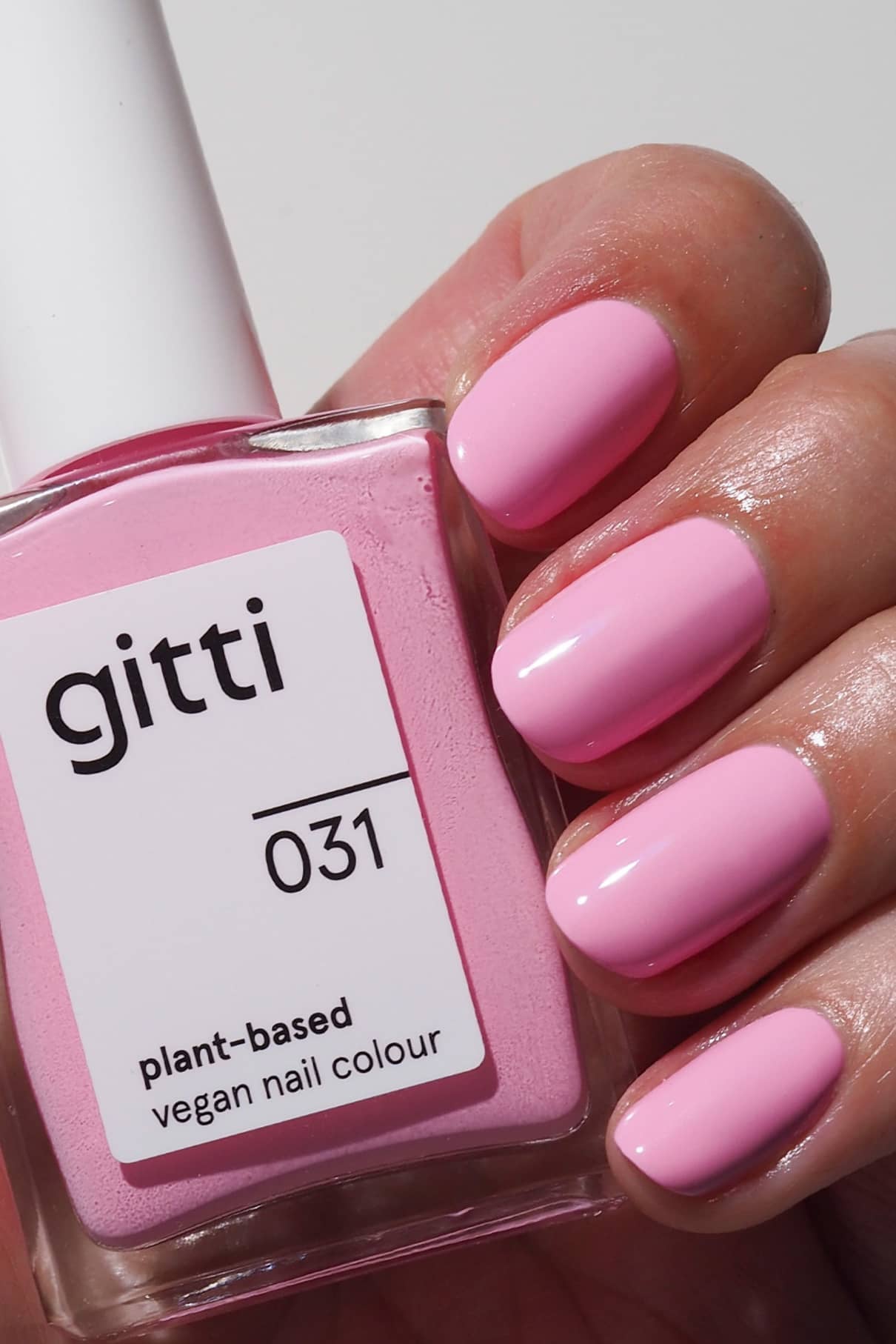 Eine Hand mit kurzen, gepflegten, in Pastellrosa lackierten Nägeln hält ein Fläschchen mit gitti no. 031, einer pflanzlichen, veganen Nagelfarbe, die in einem passenden Rosé-Ton dezente Retro-Vibes versprüht.