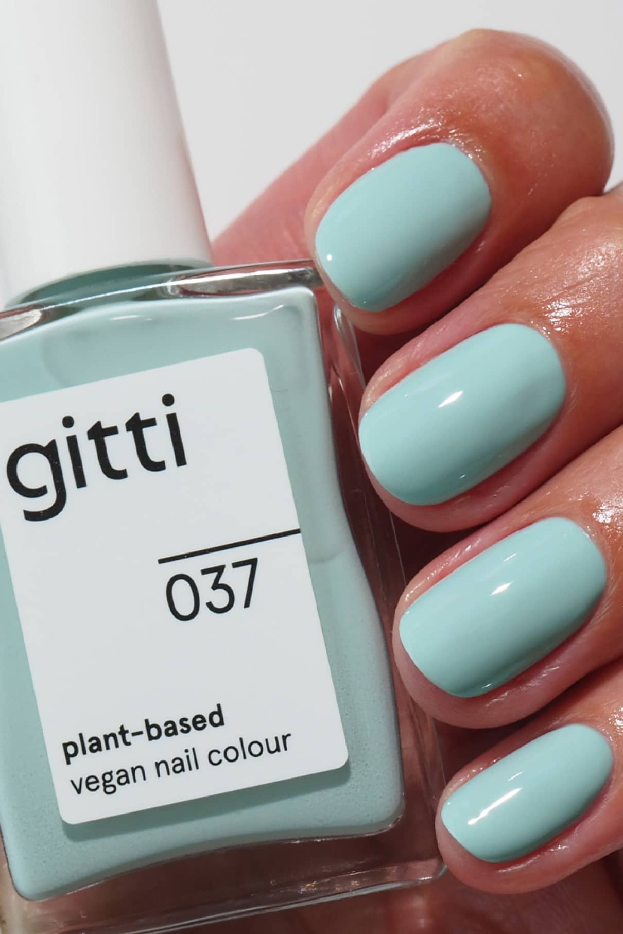 Eine Hand mit sauber manikürten hellblauen Nägeln hält das Plant Trio + Remover Set, das eine passende vegane Nagelfarbe auf Pflanzenbasis und ergänzende Über- und Unterlacke für ein makelloses Finish enthält.