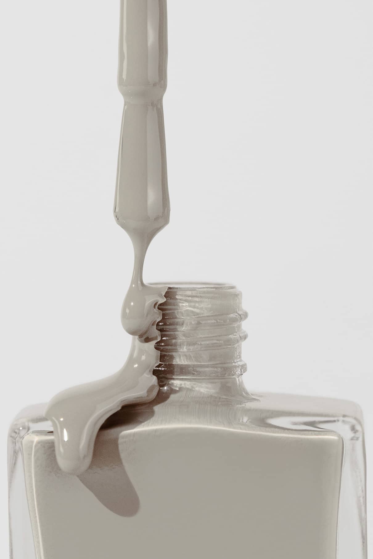 Eine Nahaufnahme eines Nagellackpinsels, der Gitti Nr. 041, ein sanftes Taupe mit grauen Untertönen, über die Öffnung und den Rand einer Klarglasflasche.