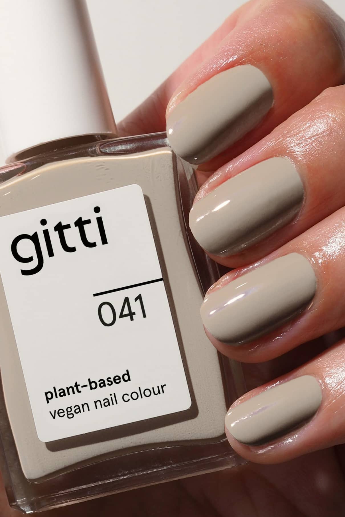 Eine Hand mit taupefarbenen manikürten Nägeln hält ein Fläschchen aus dem Plant Trio, einem veganen Nagelfarbset auf Pflanzenbasis, das sich ideal mit Top & Base Coats für ein makelloses Finish kombinieren lässt.